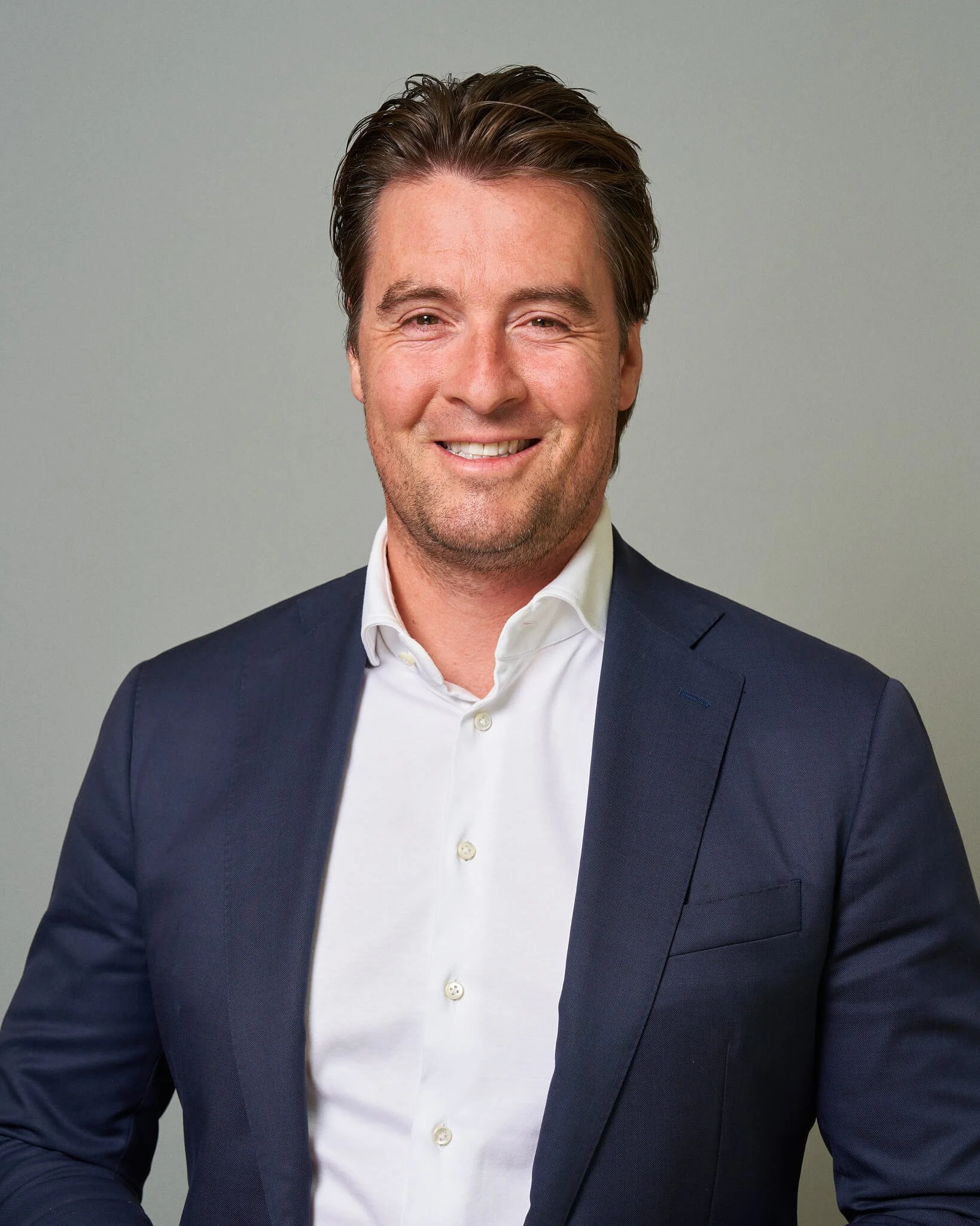 Portret van een lachende man in een donkerblauwe blazer en witte overhemd, glimlachend naar de camera.