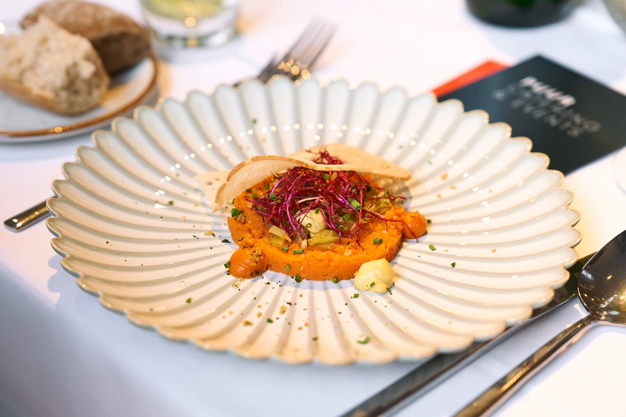 Gerecht met gepureerde zoete aardappel, garnituur, en microgroenten op een decoratief wit bord met gouden rand.