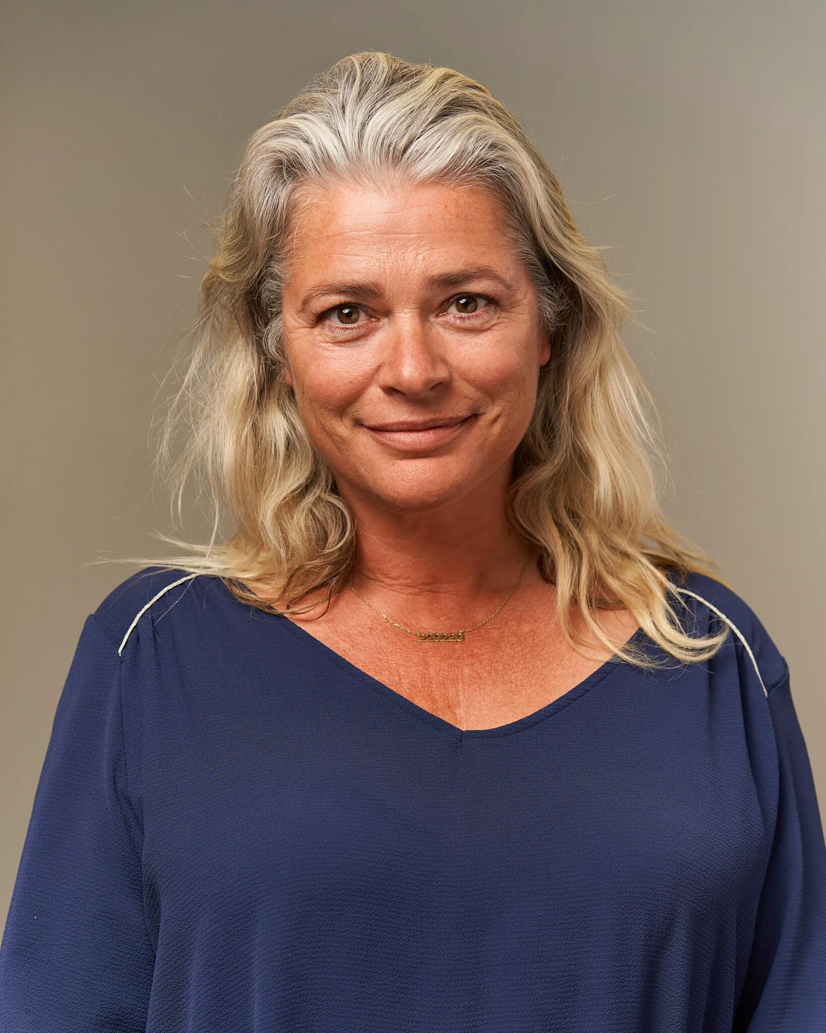 Portret van een lachende vrouw met grijs haar en blauwe jurk. Gefotografeerd door een professionele portretfotograaf.