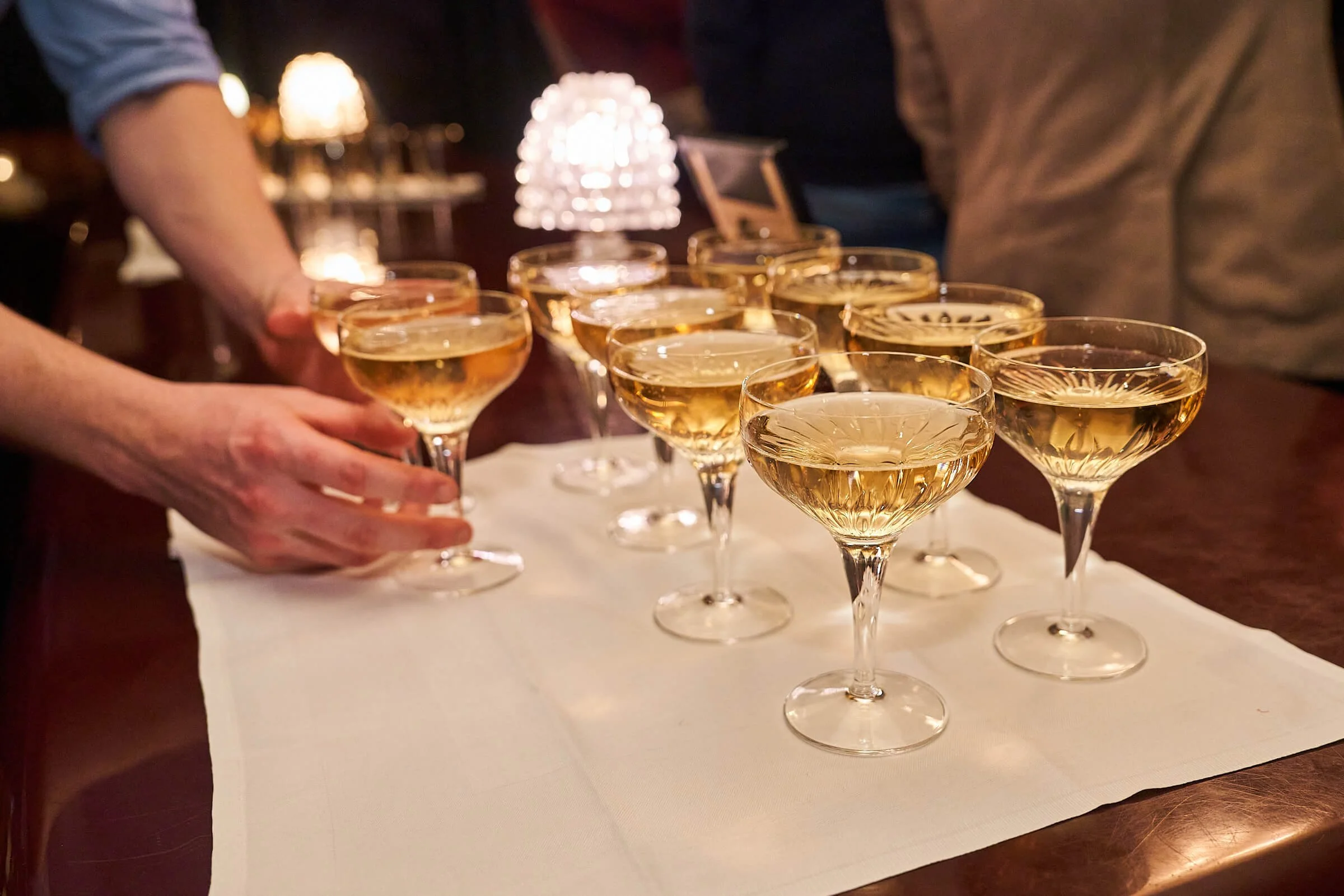 Verschillende champagneglazen gevuld met champagne op een zilverkleurige dienblad op een bar in een bar of restaurant.