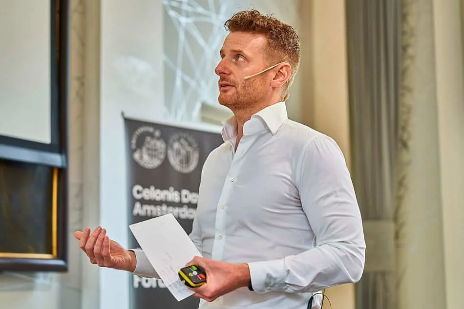 Man met een wit overhemd en een headset die een presentatie geeft in een kamer met gordijnen.