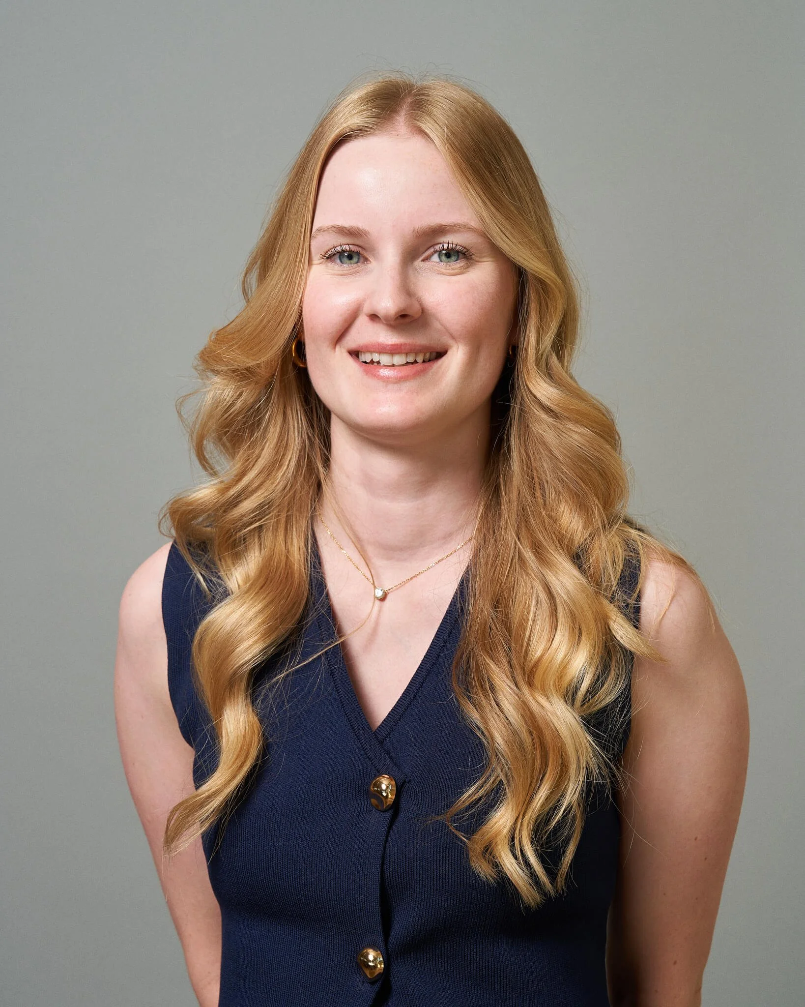 Portret van een lachende vrouw met golvend rood haar, zittend tegen een effen lichte achtergrond.