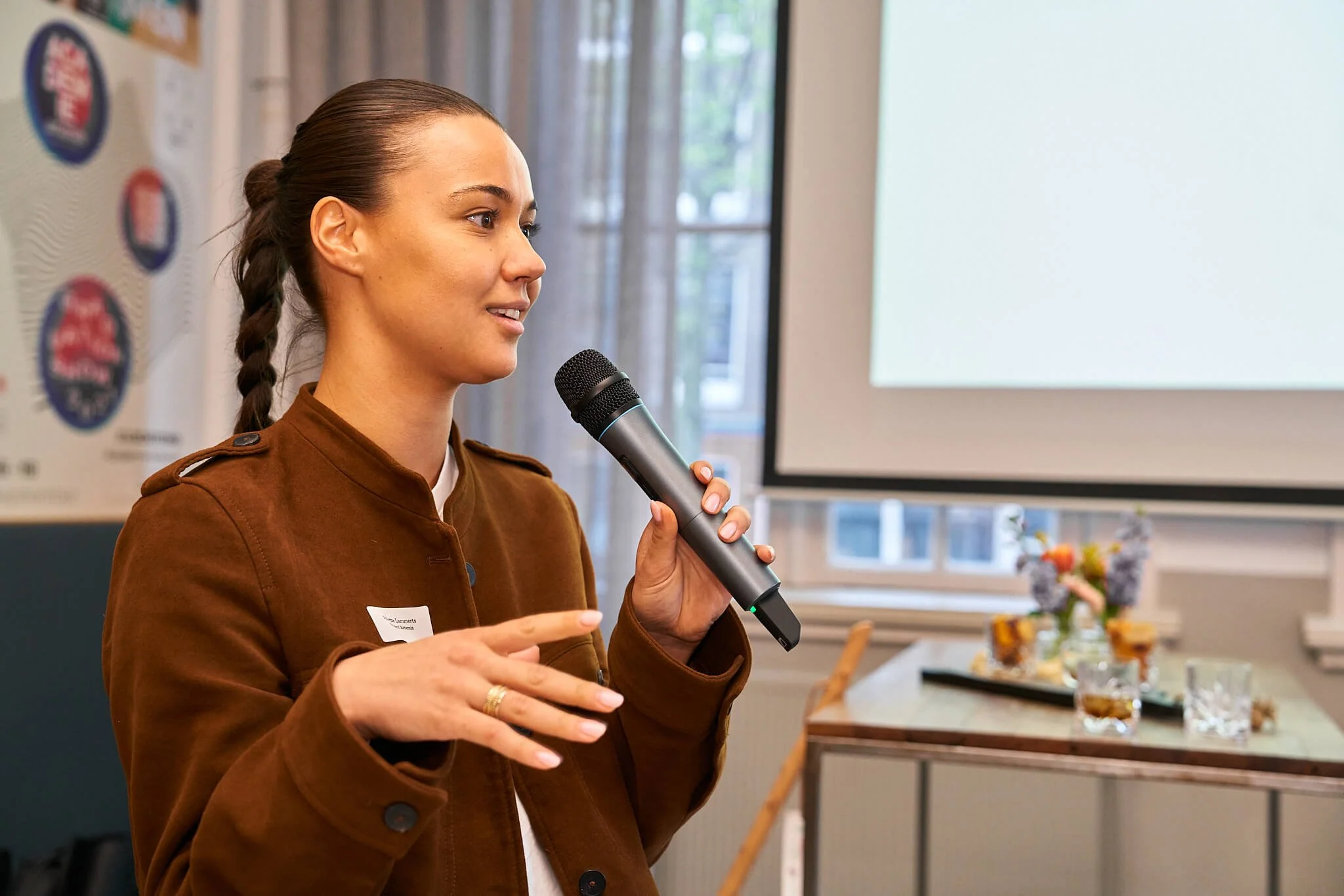 Vrouw geeft presentatie met microfoon in een vergaderzaal, achtergrond met bloemen en projection