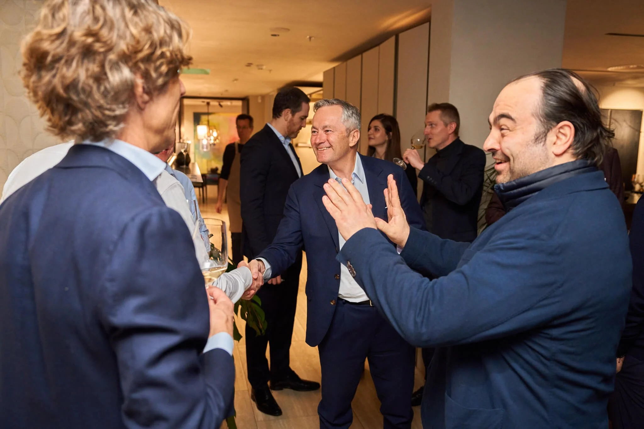 Mensen die elkaar begroeten en praten tijdens een sociale bijeenkomst, sommige met drankjes in hun handen.
