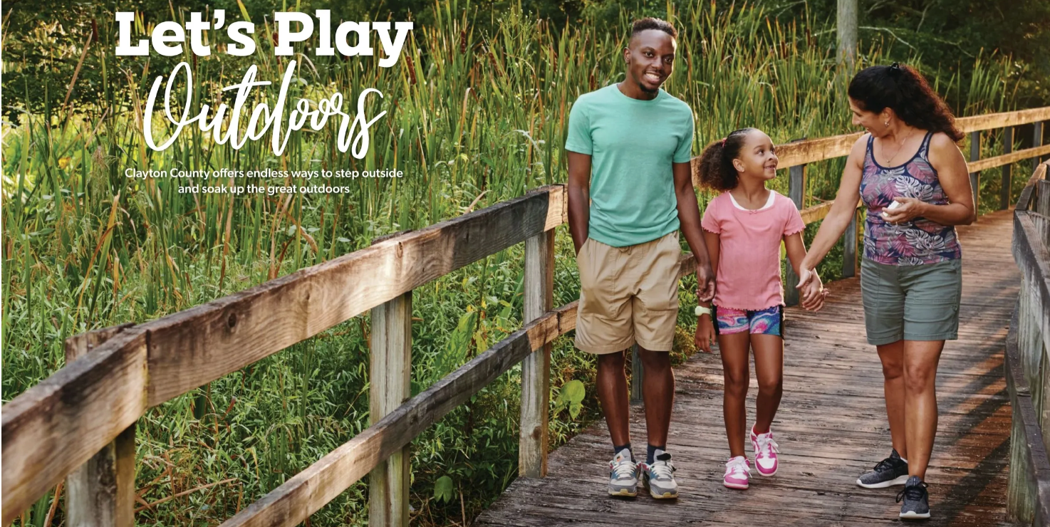 A family of three walking on a wooden boardwalk surrounded by green plants, smiling and enjoying outdoor activities in Clayton County's tourism.
