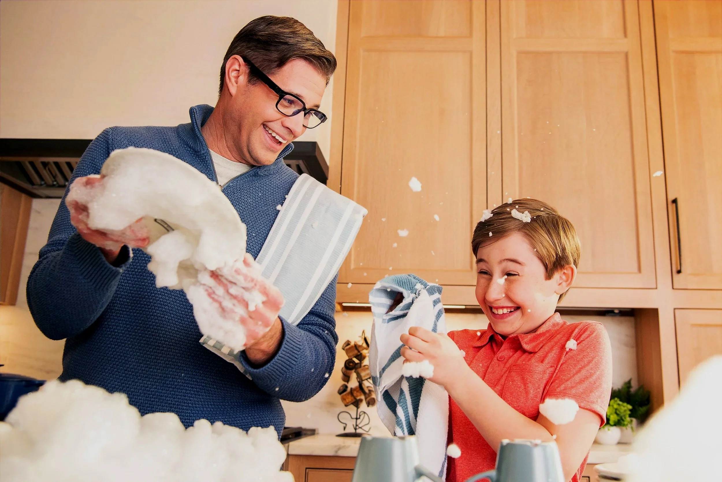 Echo Frames by Amazon. A man and a boy having fun with whipped cream in a kitchen, playing and laughing as whipped cream splatters around.