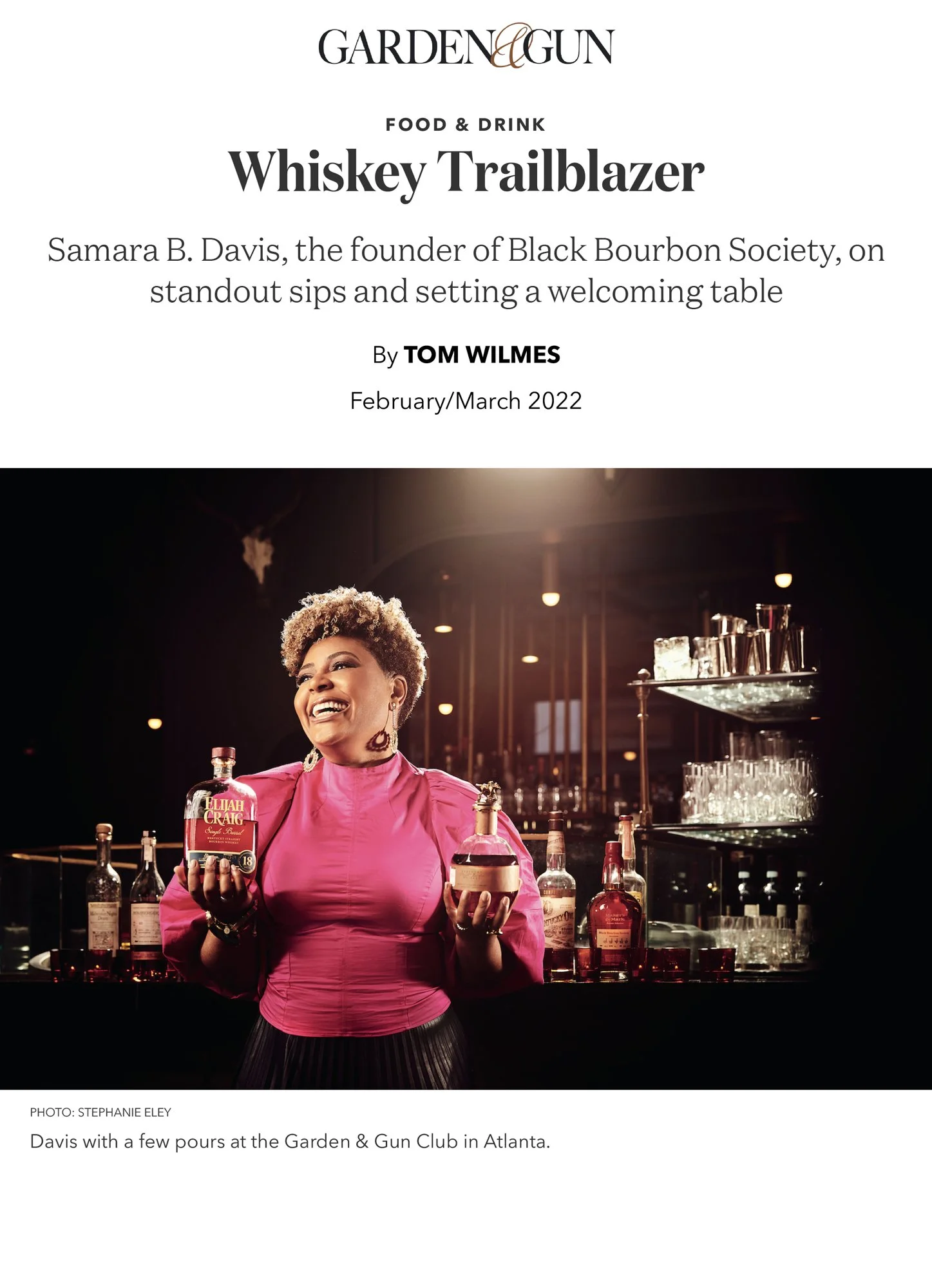 Cover page of Garden & Gun with a woman smiling and holding two bottles of alcohol, standing in a bar setting. The woman is wearing a pink dress. The background shows shelves with glasses and liquor bottles.