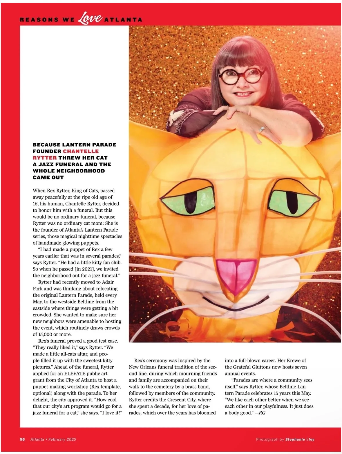 Woman with glasses smiling resting her arms on an orange pumpkin-shaped lantern with a cat face design, Halloween-themed decoration with glittery background.