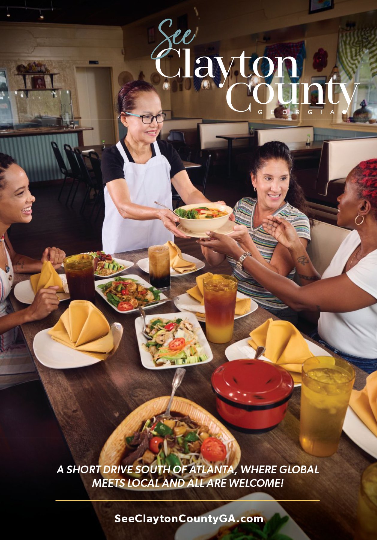 Four women sitting at a restaurant table with colorful dishes, drinks, and a server handing out a bowl of food, with a sign promoting travel and tourism ikn Clayton County, Georgia.