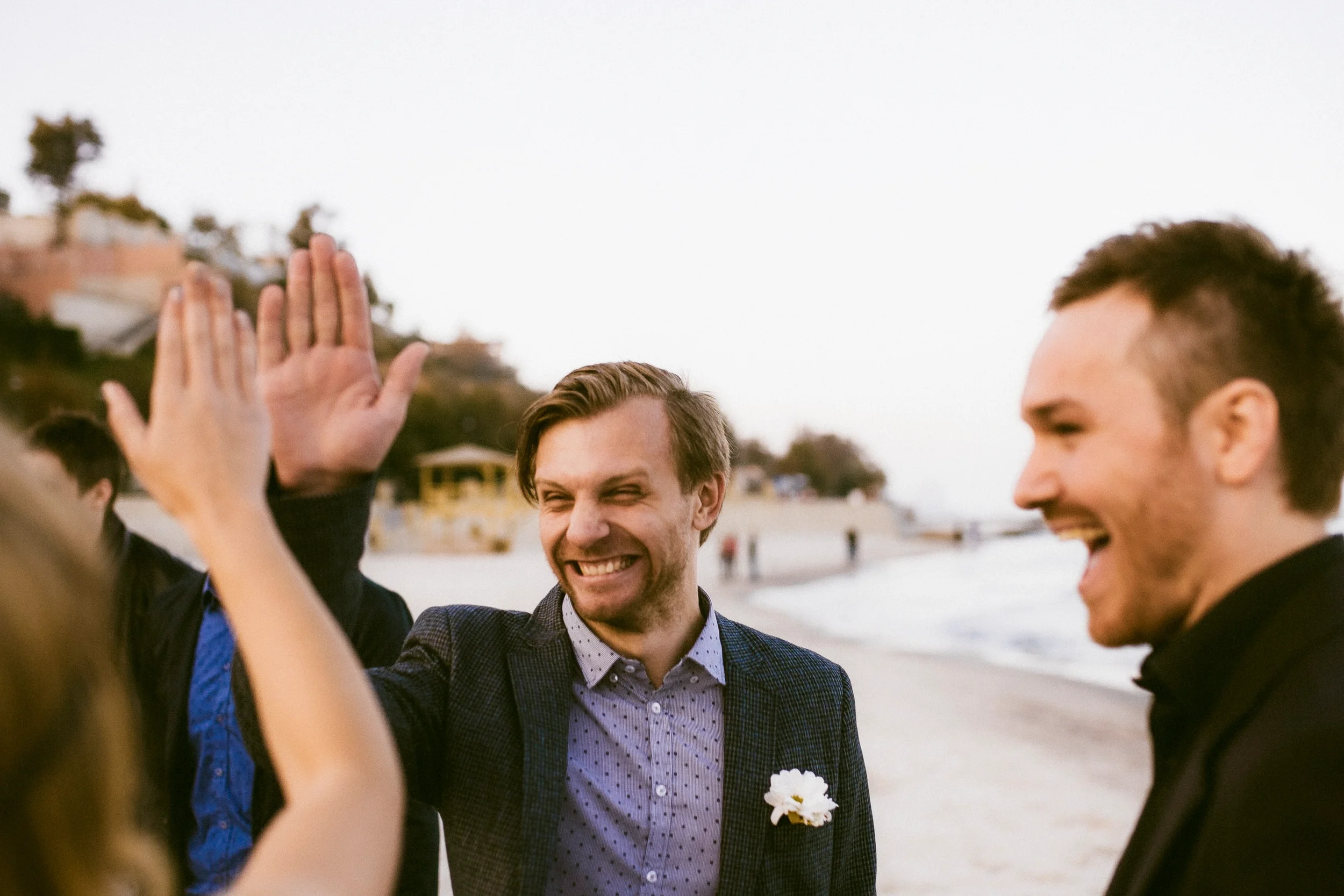 Gruppe junger Männer macht High Five am Strand, lachend, im Freien bei Sonnenuntergang.