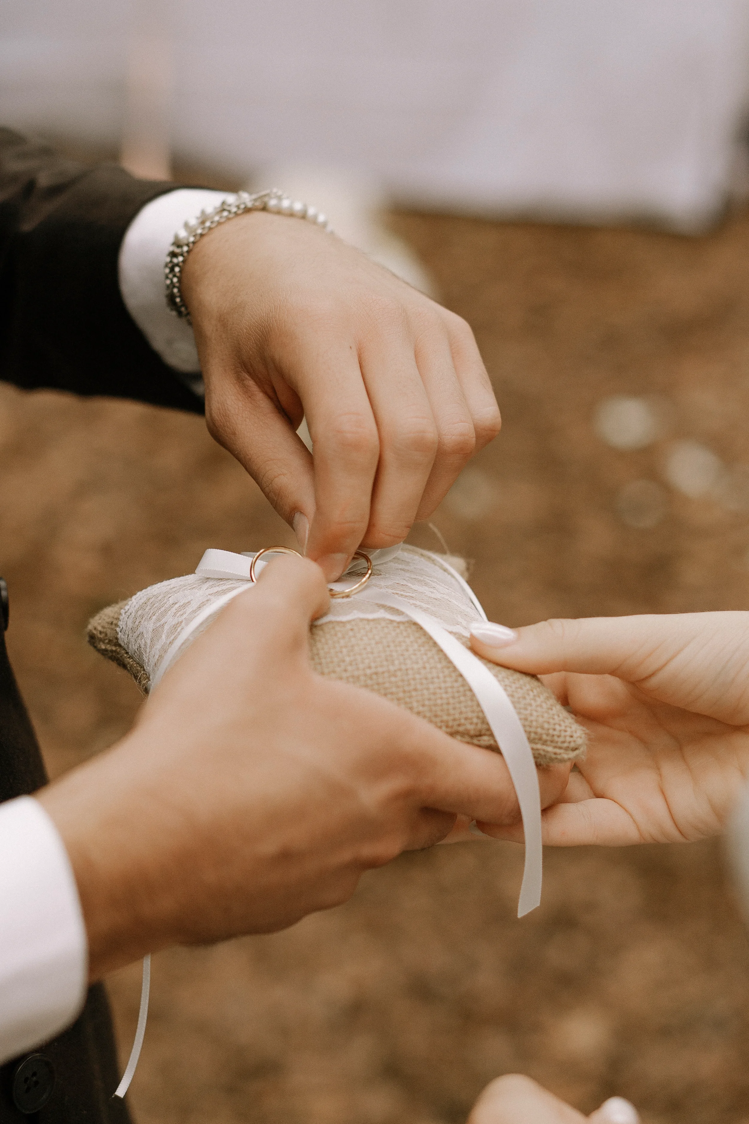 Hand, die eine Ring auf einem weißen Schuh anlegt, während andere Hand den Schuh hält, bei einer Hochzeitszeremonie.