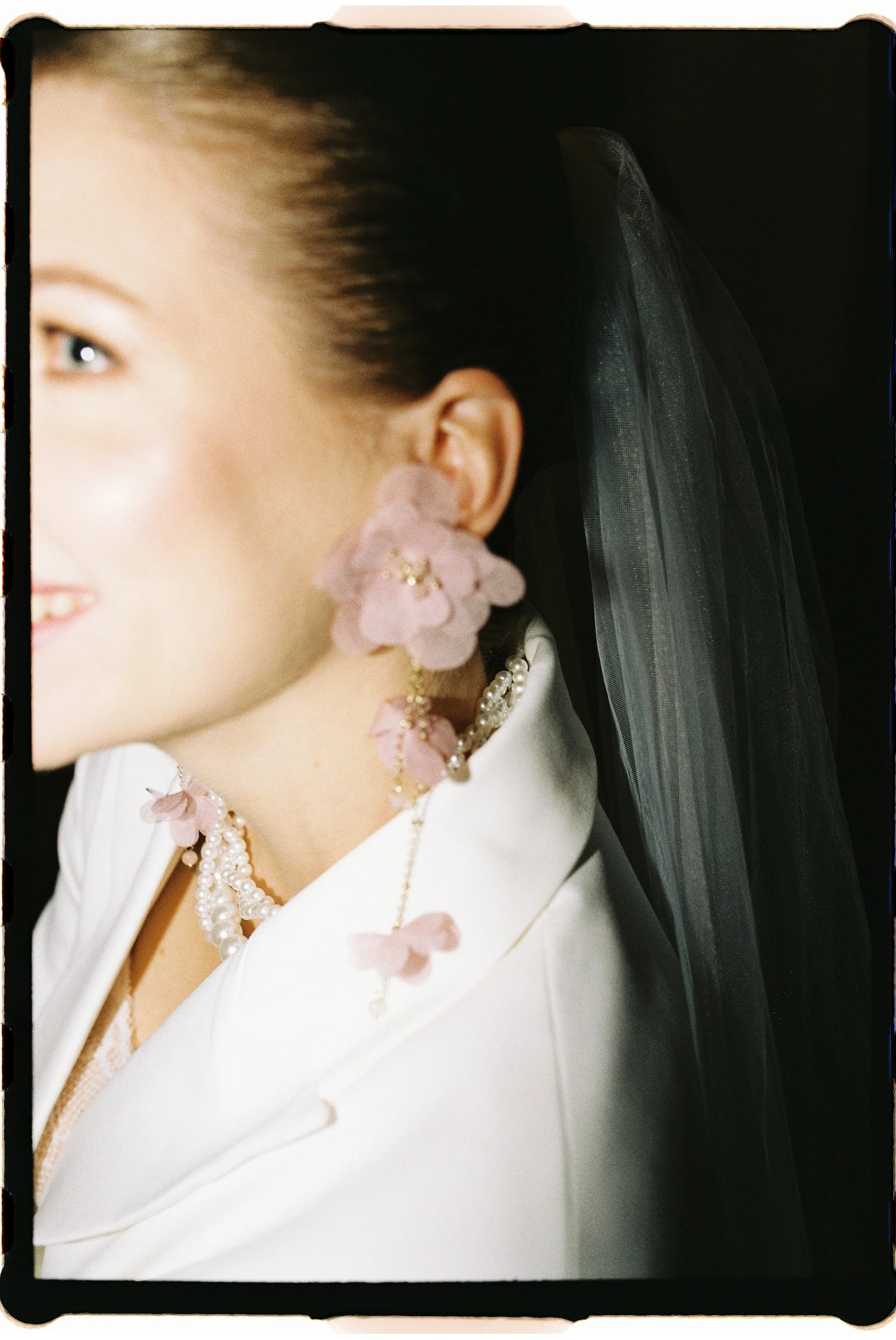 Nahaufnahme eines Frauengesichts mit Schmuck, auf dem Bild sind eine Perlenkette, eine große Blumenohrring und ein weißer Kleid zu sehen.