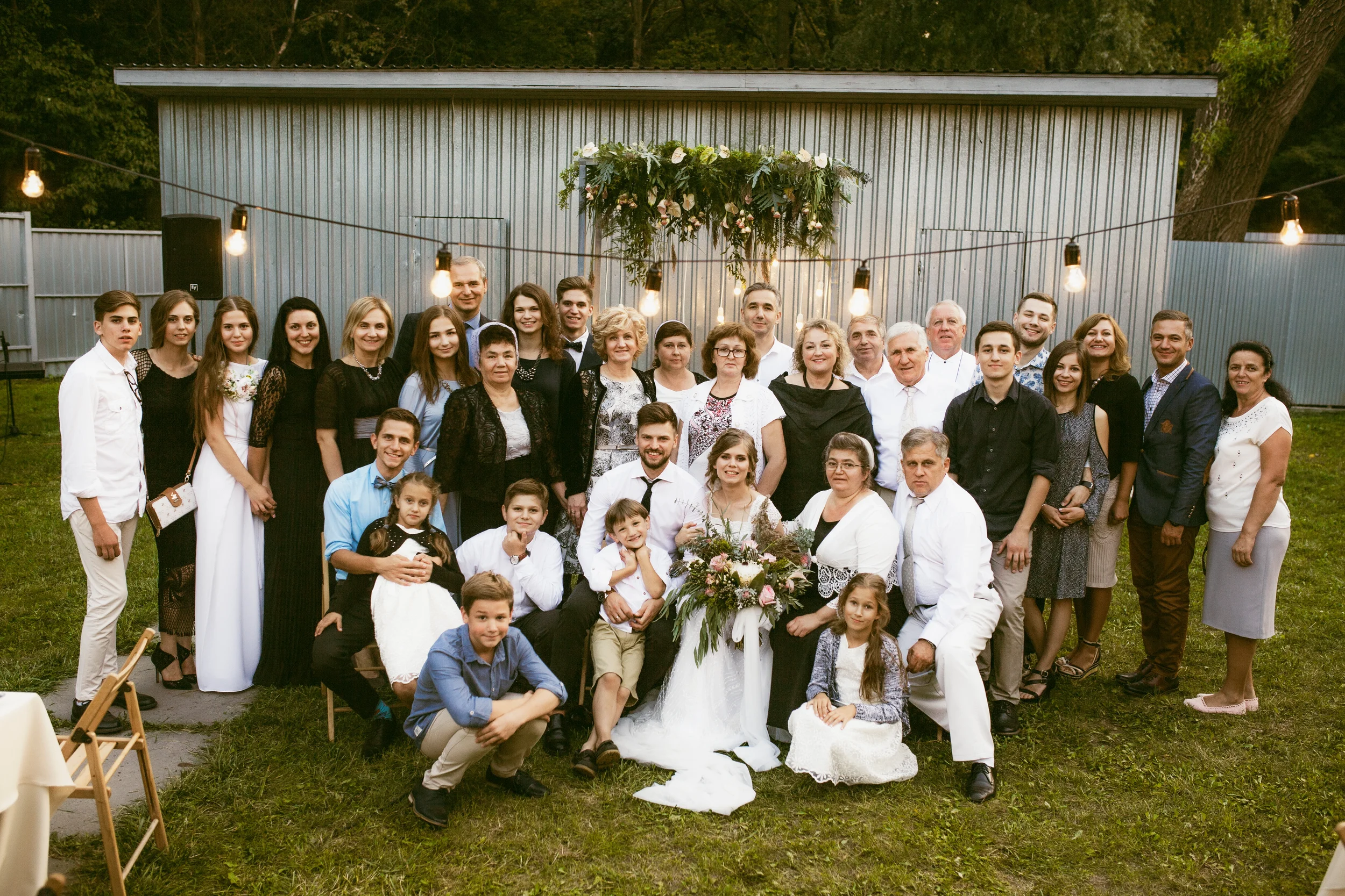 Gruppenfoto einer Familie bei einer Feier im Garten, mit viel Lichtern und Blumen, alle lächeln.