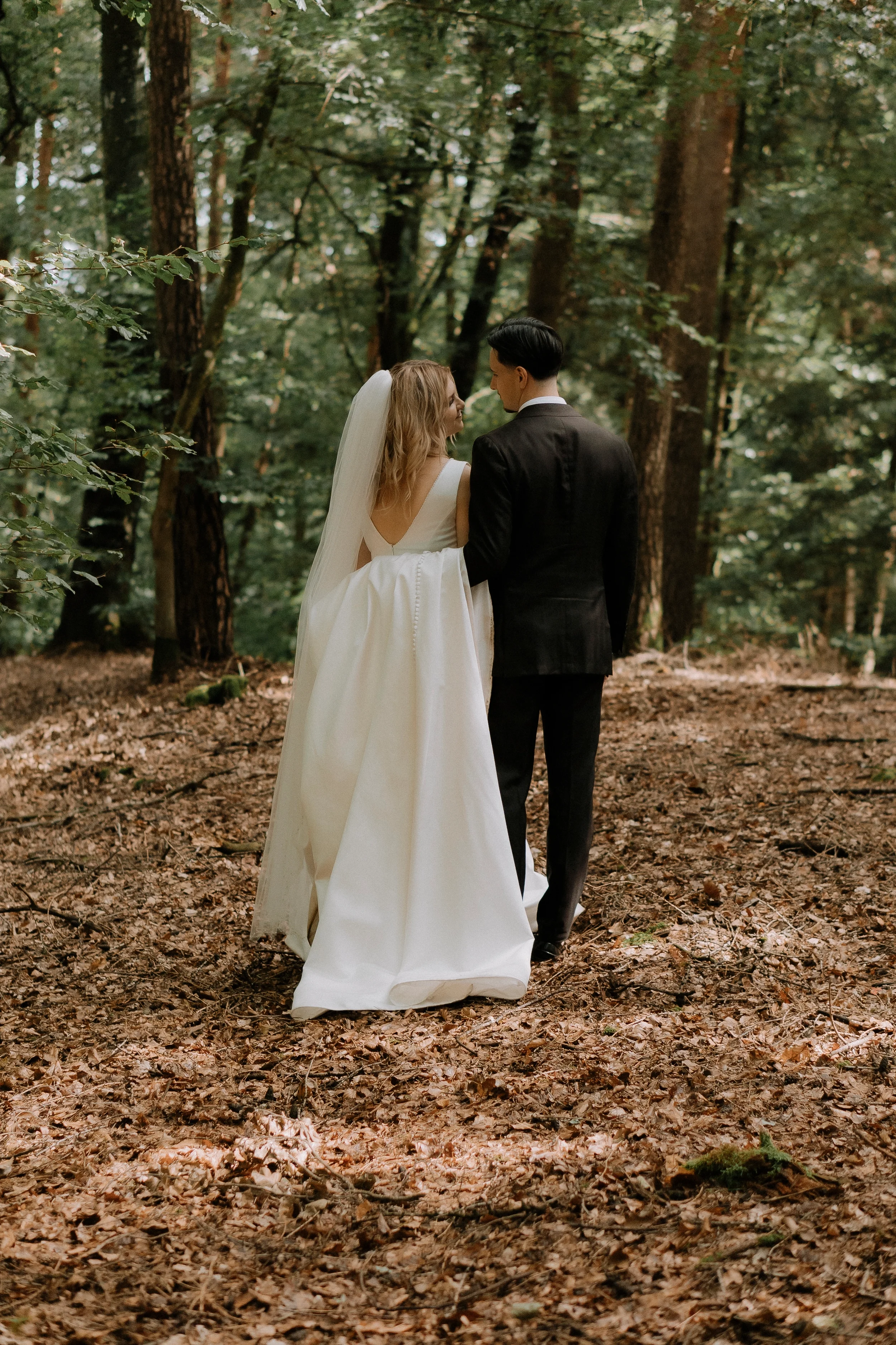 Ein Brautpaar in formeller Kleidung, die in einem Wald stehen, die Frau trägt ein weißes Brautkleid mit Schleier und der Mann trägt einen schwarzen Anzug.