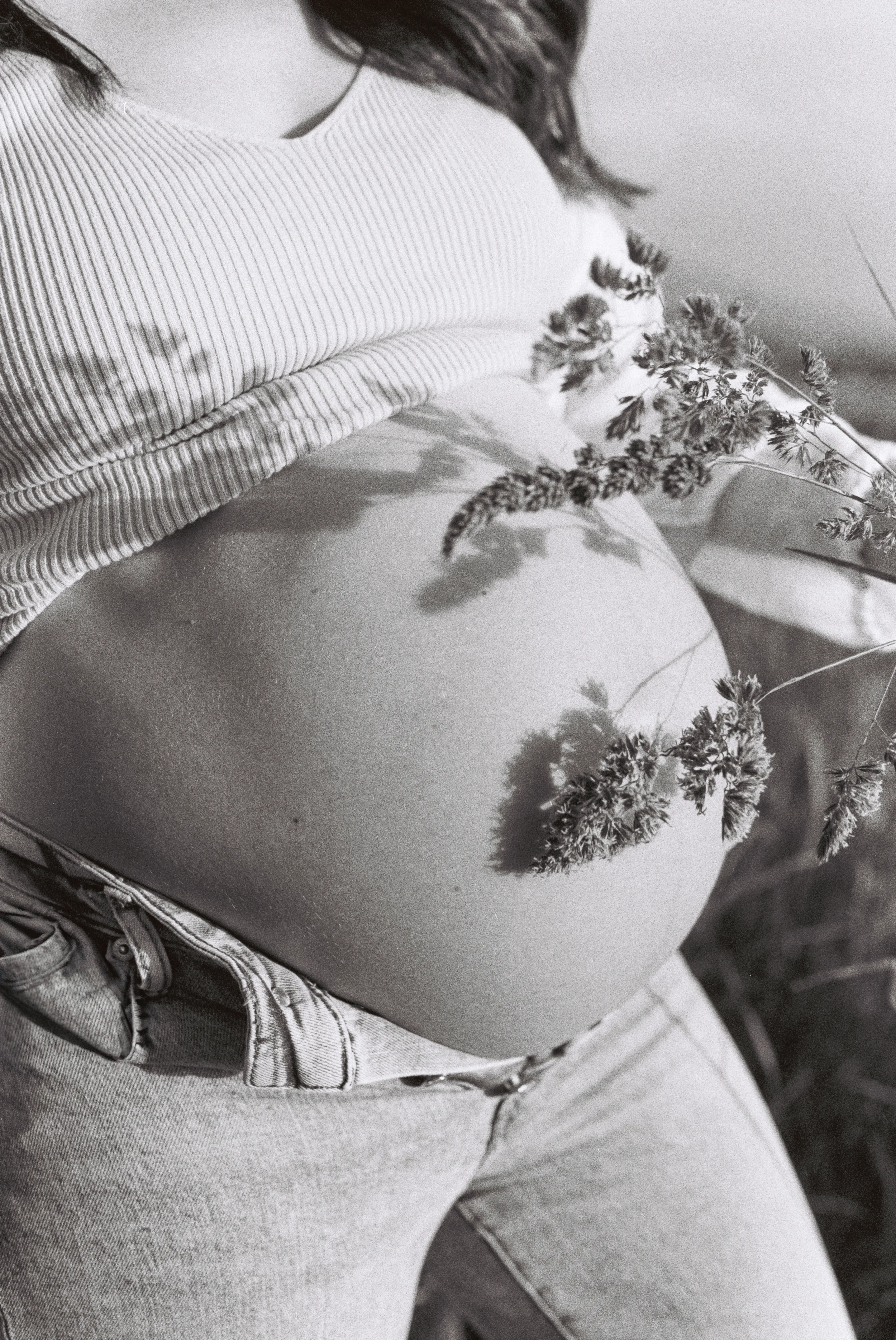 Schwarz-weiß-Foto einer gebärenden Frau mit sichtbarem Babybauch, die auf einem Bett liegt, trägt ein gestreiftes Oberteil und Jeans, mit Blumen vor ihrer Brust.