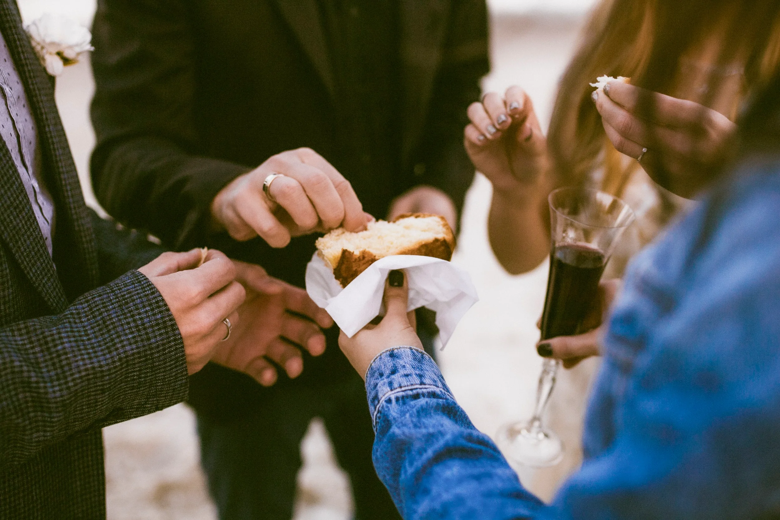 Menschen teilen Kuchen und Wein bei einer Feier, Nahaufnahme der Hände und Getränke.