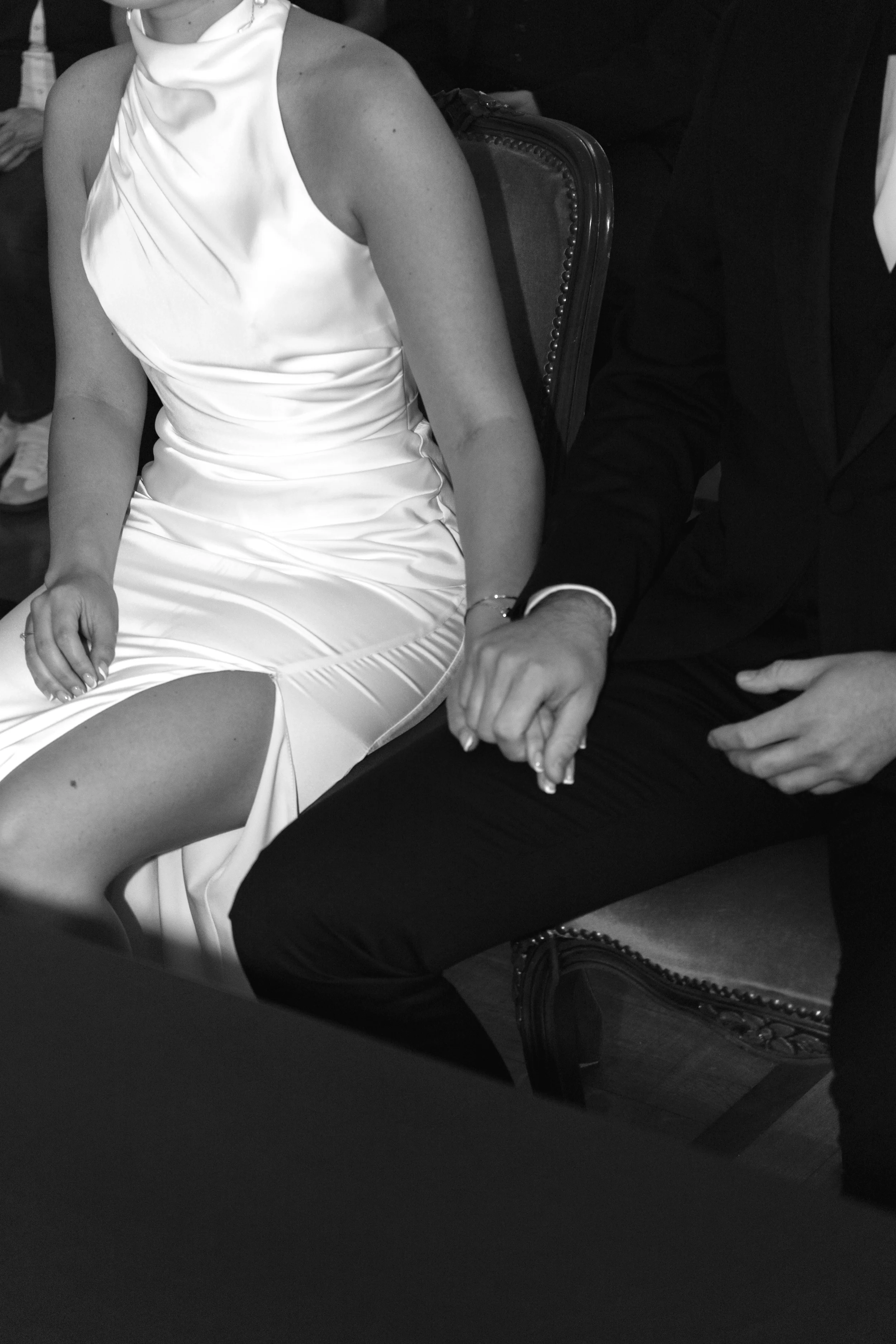 Schwarzes und weißes foto eines Mannes und einer Frau, die zusammen sitzen und Hände halten, die Frau trägt ein weißes Kleid, der Mann trägt einen schwarzen Anzug, das Bild ist teilweise sichtbar