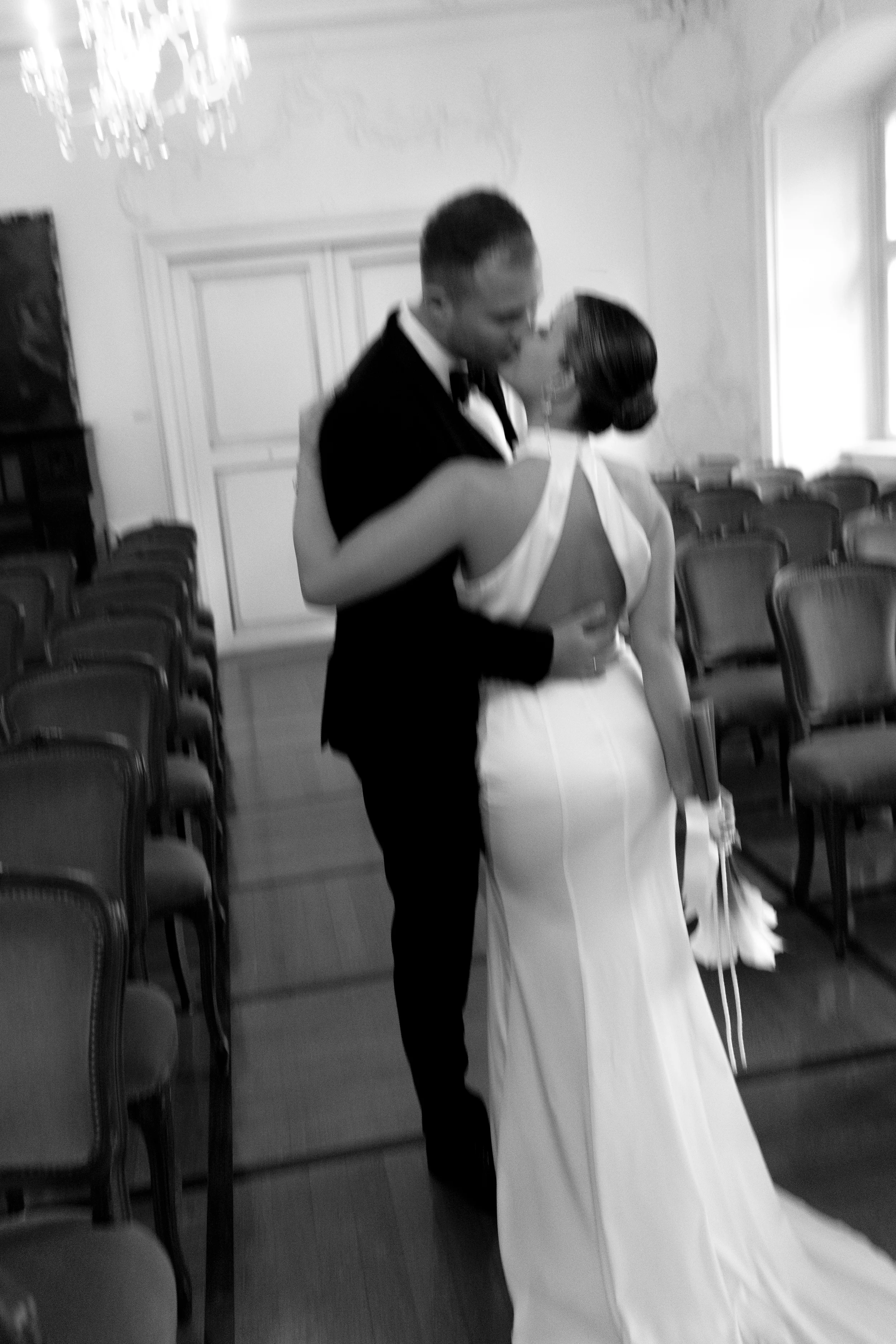 Ein Paar, das sich bei einer Hochzeit küsst, während sie in einem großen, leeren Saal mit Stühlen steht.
