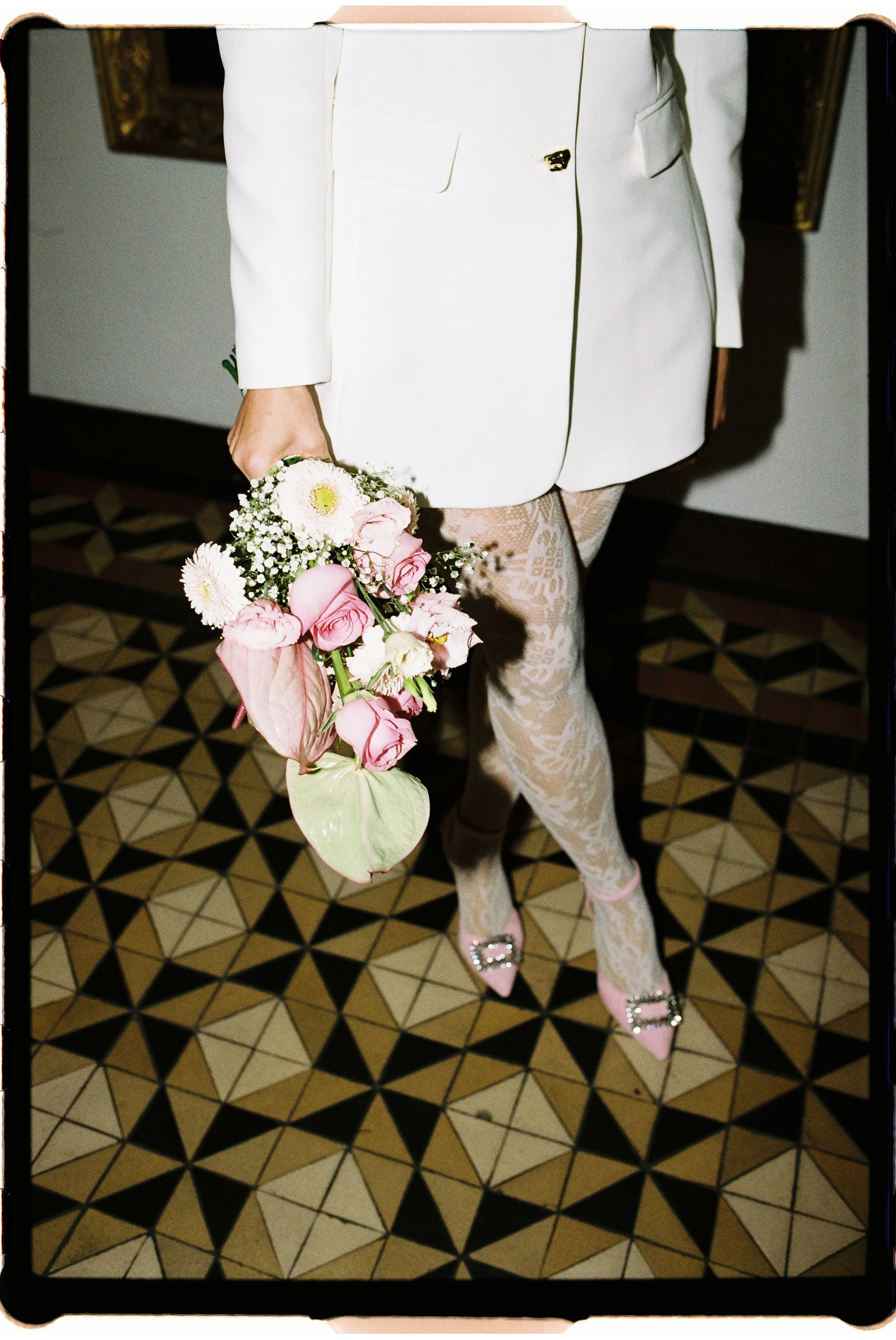 Detailaufnahme einer Braut mit rosa Brautstrauß, weißem Blazer und Spitze während einer standesamtlichen Hochzeit.