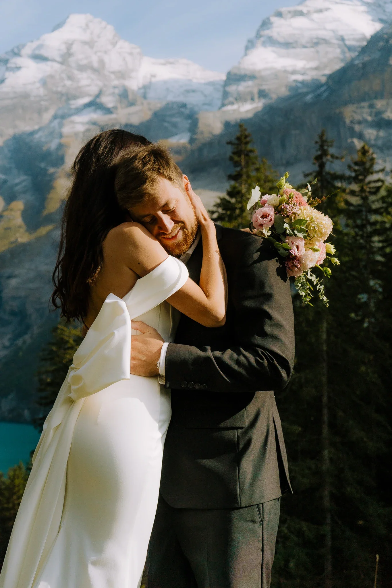 Ein glückliches Brautpaar im Freien vor einer Gebirgskulisse, umarmt sich herzlich, die Braut trägt ein weißes Kleid und die Trauung findet wahrscheinlich im Sommer statt.