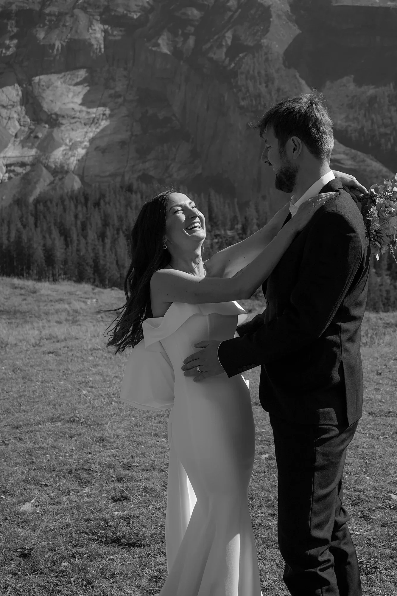 Ein lächelndes Paar bei einer Hochzeit im Freien, mit Bergen im Hintergrund, schwarz-weiß