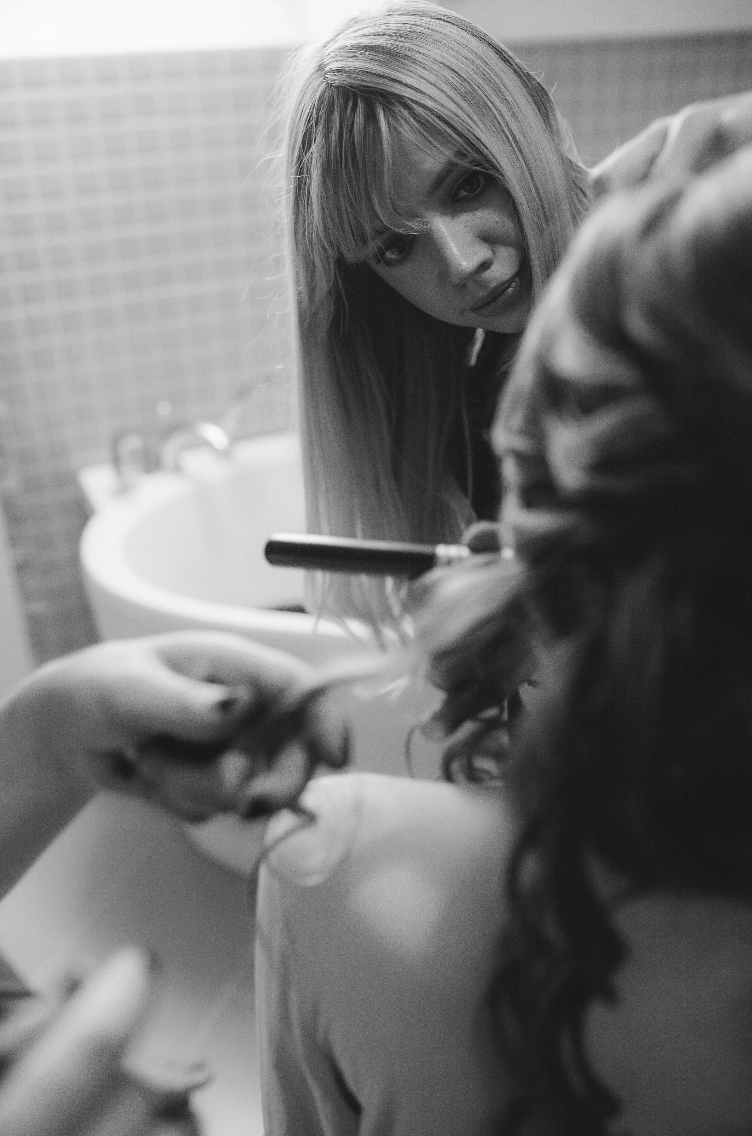 Schwarzes und weißes Foto einer Frau mit langen Haaren, die in einen Spiegel schaut, während sie ein Handy hält.