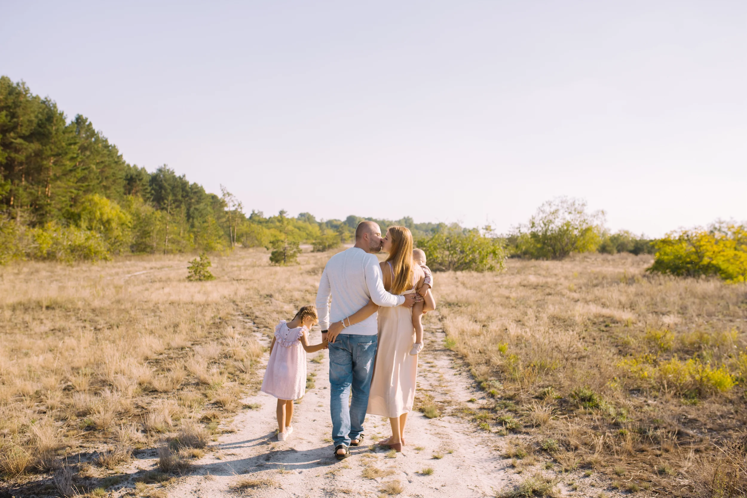 Familie auf einem Feld bei Sonnenuntergang, bestehend aus zwei Erwachsenen und drei Kindern, die sich küssen und spielen.