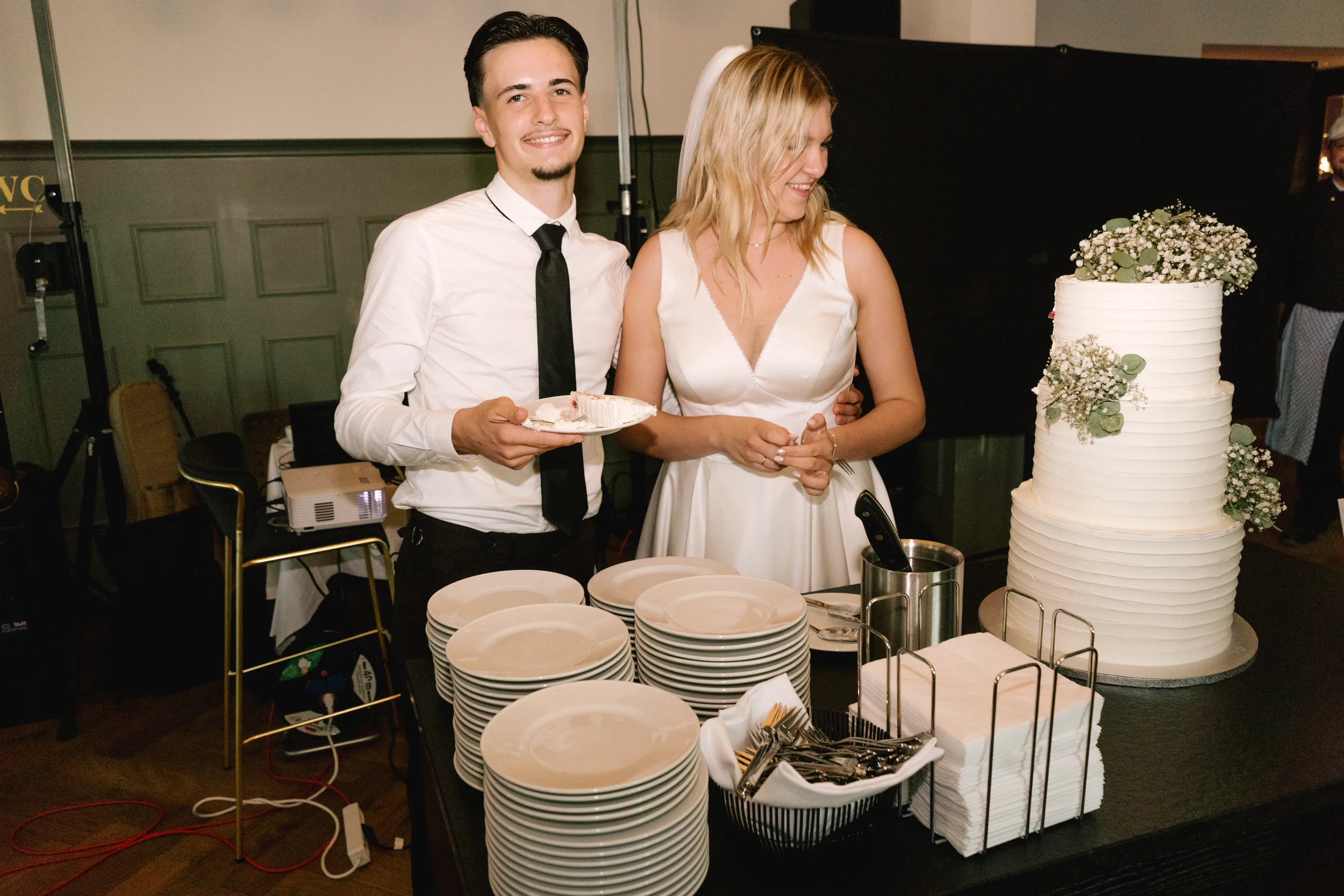 Ein junges Paar in Hochzeitskleidung beim Kuchen schneiden bei einer Feier.