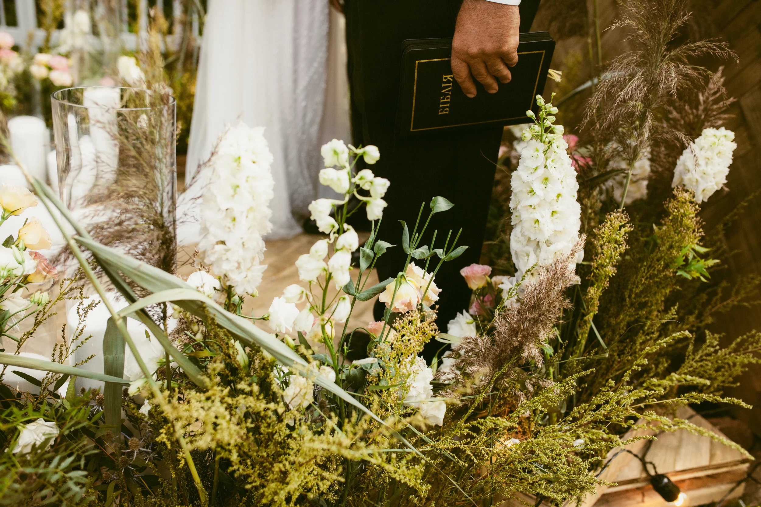 Eine Person hält eine schwarze Bibel in der Hand, während sie sich an einem Blumenarrangement bei einer Zeremonie oder einem Gottesdienst beteiligt.