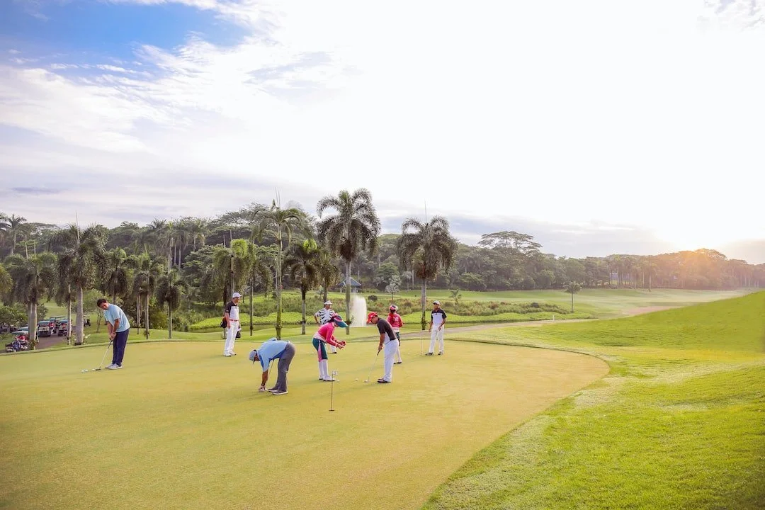 A large family practicing their putt shots on the putting practice green in a tropical environment