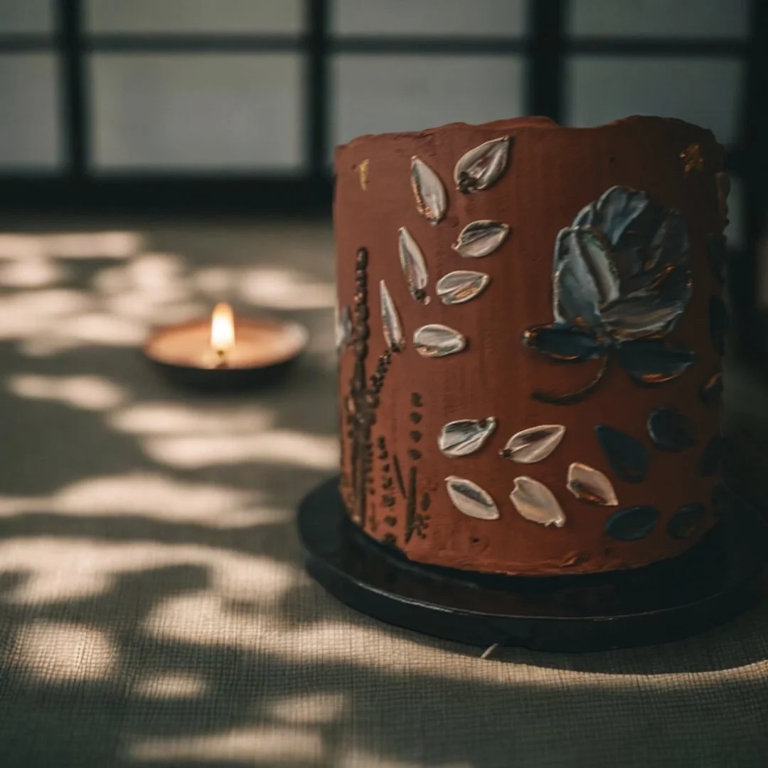 Terracotta buttercream cake with sculpted floral details and leaf accents on a dark cake stand
