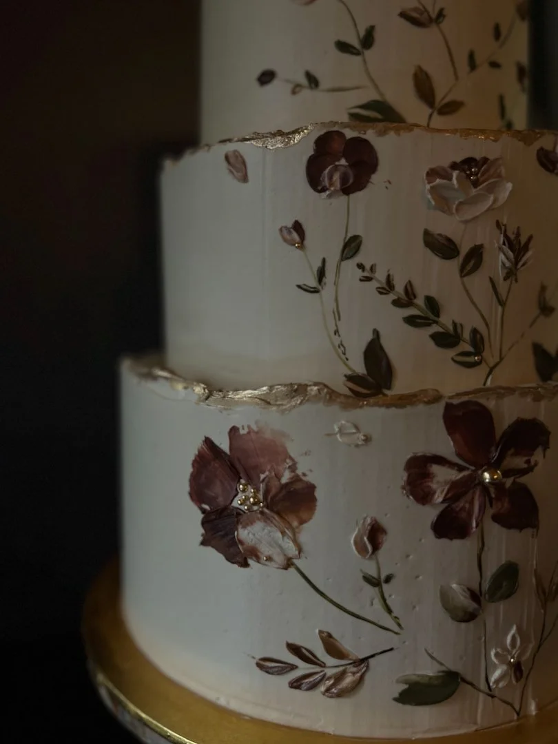 A 3-tier wedding cake with a cream background color and moody deep romantic colors on buttercream flowers