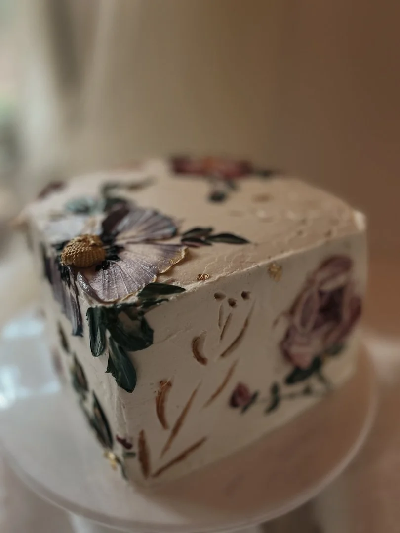 Hand-painted floral cake with soft white buttercream and lavender blooms on a white stand, Grand Rapids, MI