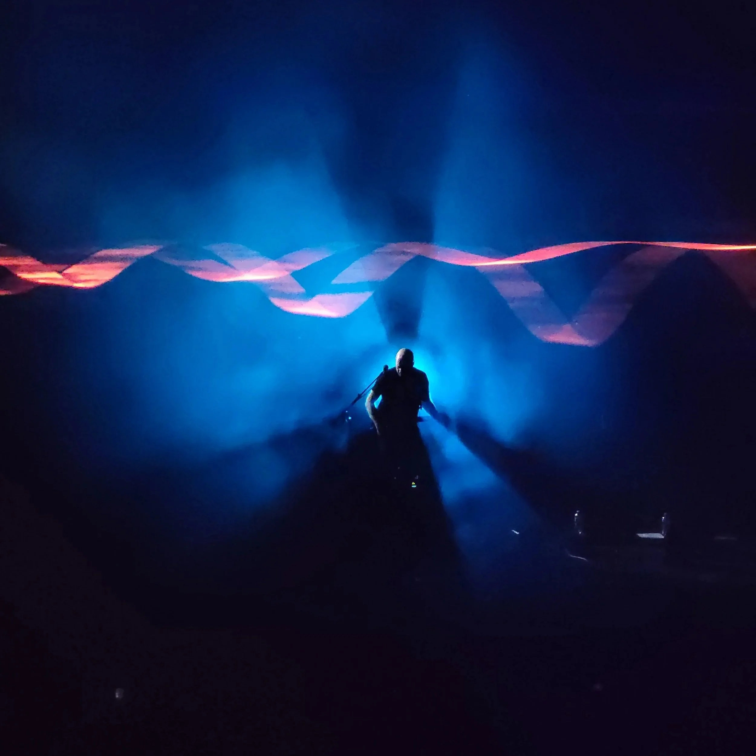 The guitarist of the band Brit Floyd standing on stage with blue lighting against a dark background with abstract light patterns.