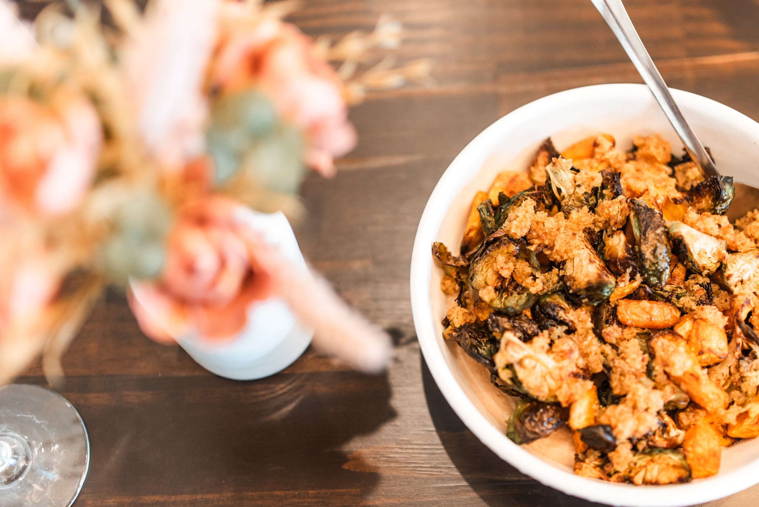 Bowl of roasted or fried vegetables, possibly including eggplant, with a spoon inside, placed on a dark wooden table.