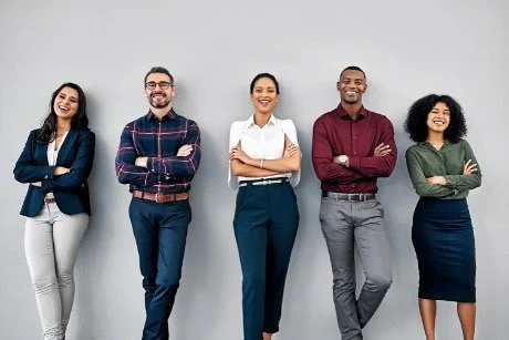 3 women and 2 men of different ethnicities in business casual clothing, smiling and standing against a wall