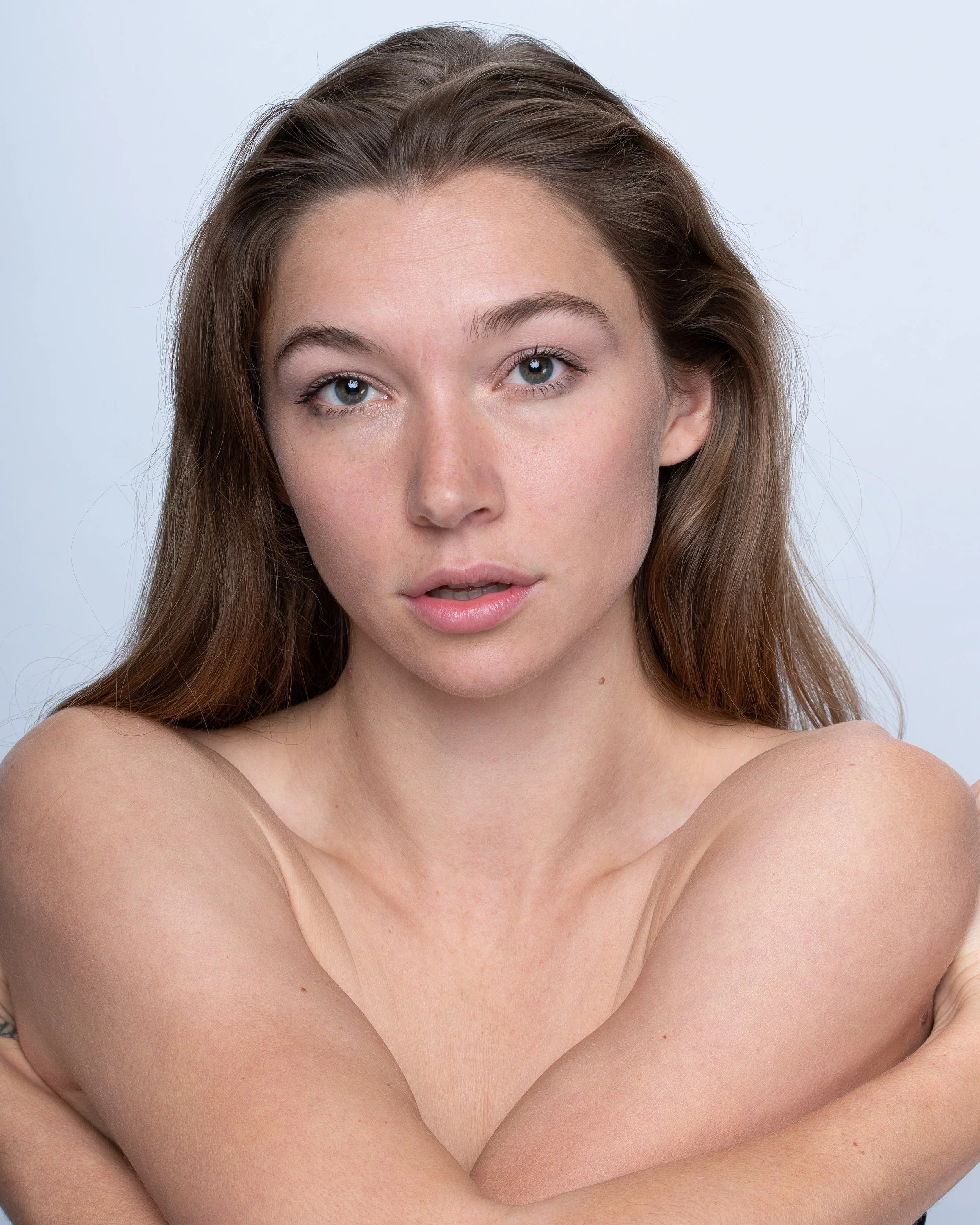 Close-up portrait of a young woman with long, brown hair and light skin, looking directly at the camera with a neutral expression.