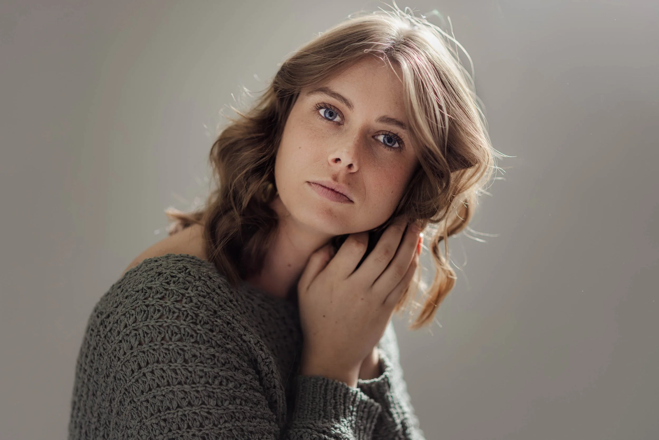 a soft lit portrait of a woman holding her hands to her head