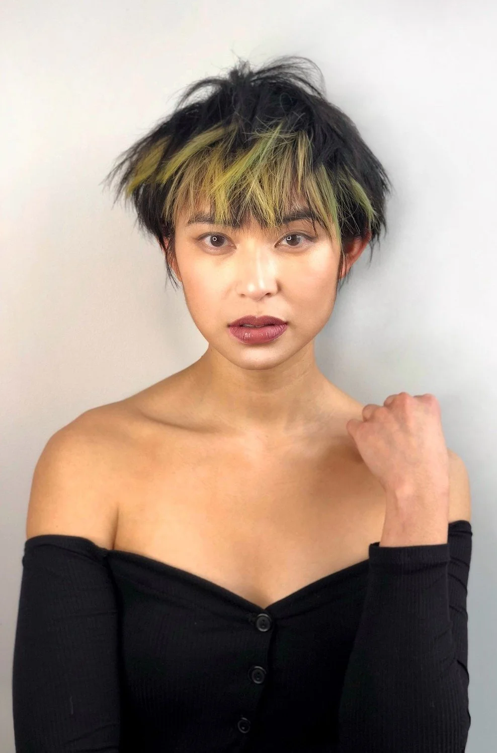 A young woman with a trendy pixie haircut in pastel colors gently touching her shoulder.