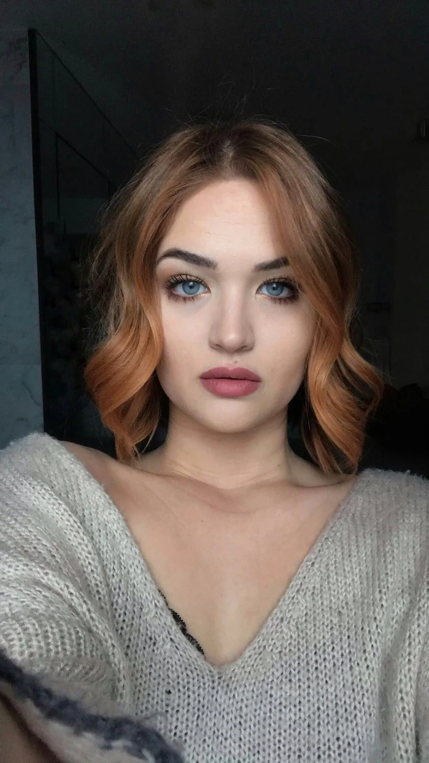 Portrait of a woman with red hair, blue eyes, wearing a beige sweater.