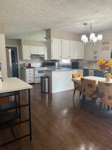 Kitchen and dining area with white cabinets, wooden floors, a dining table with four patterned chairs, and a small kitchen island.