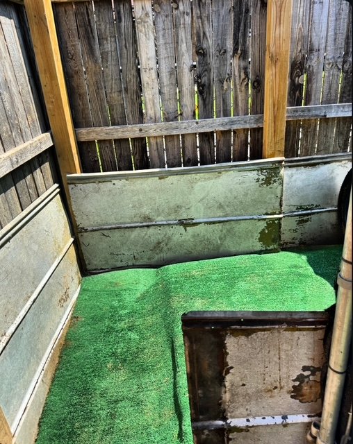 Small outdoor space with rusty metal panels, a wooden fence, and a patch of green artificial turf.