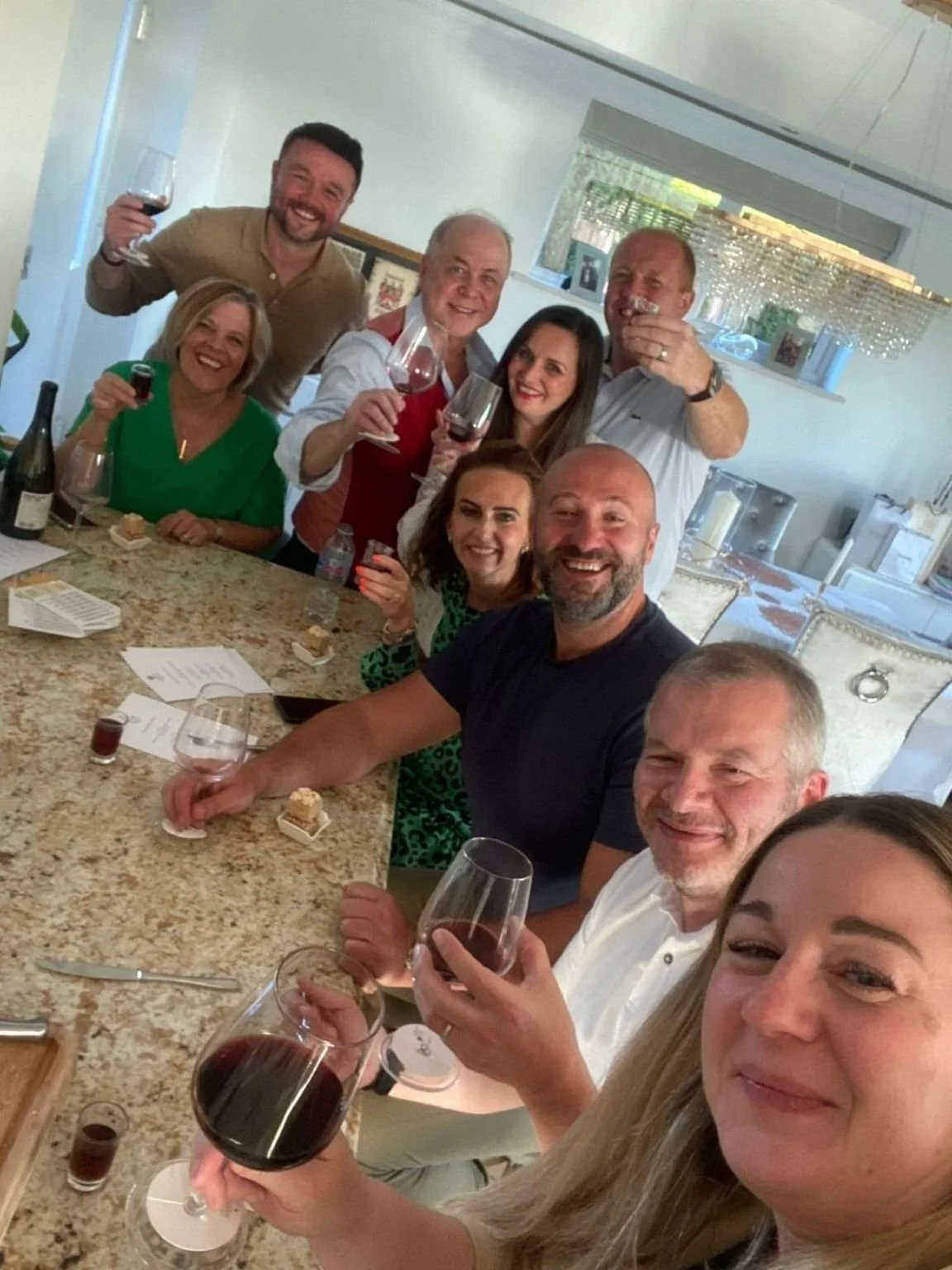A lively group of friends smiling and raising glasses of red wine during a premium private wine tasting experience hosted at home in Merseyside.