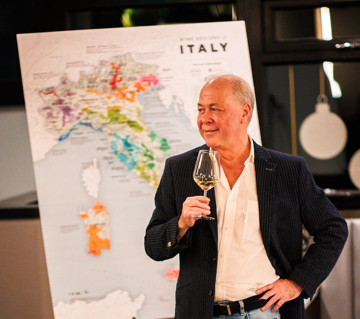 Wine Director from Colby Wines holding a glass of wine in front of an Italian wine map during a bespoke tasting experience.