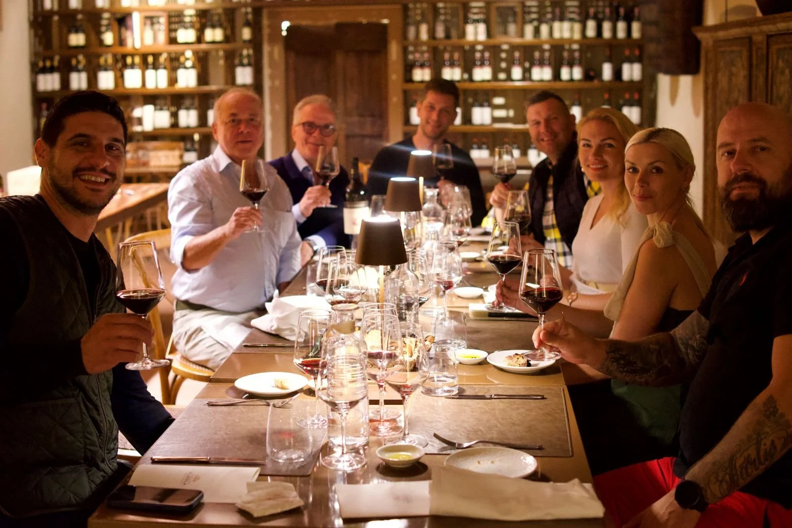 An executive group enjoying an exclusive corporate wine tasting dinner inside a rustic vineyard cellar in Tuscany, raising glasses of premium red wine.