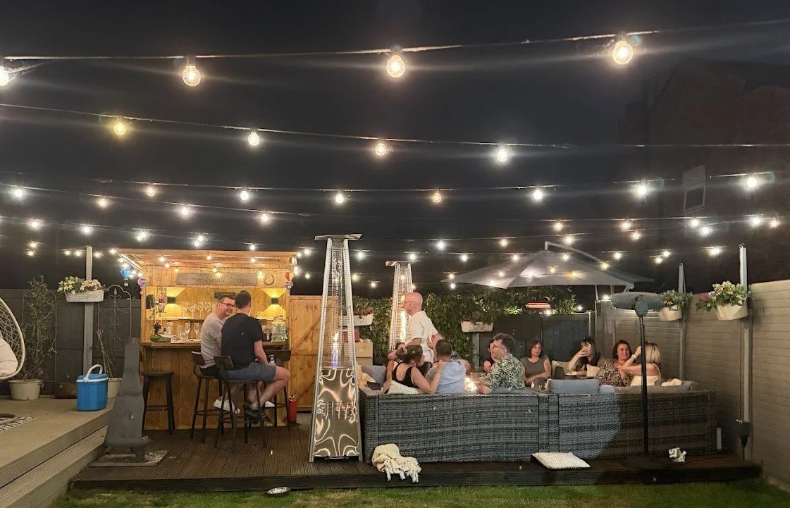 An outdoor private home wine tasting experience with guests gathered under festoon lights in a beautifully styled garden on The Wirral, curated by Colby Wines.