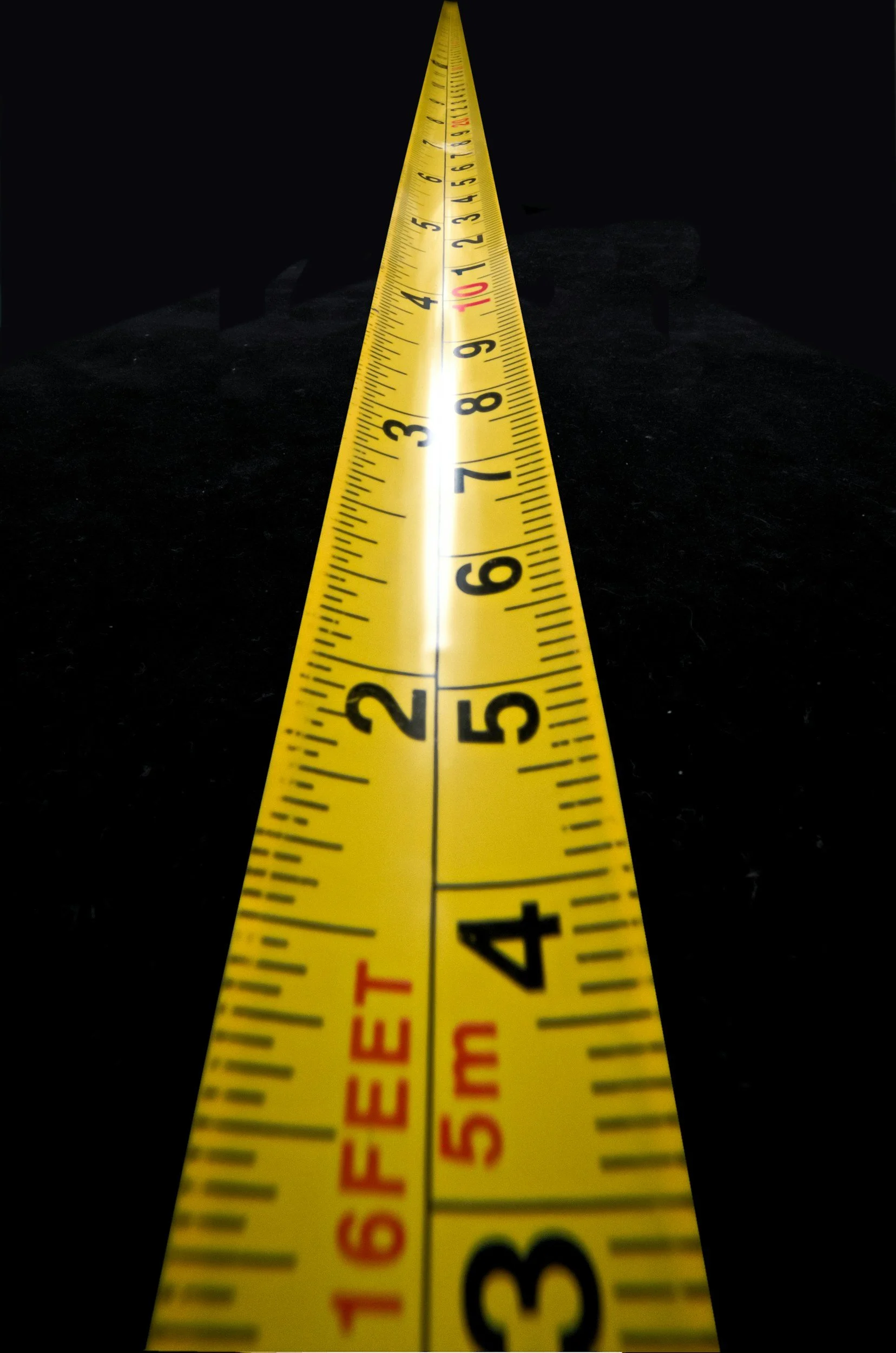 Close-up view of a yellow measuring tape placed on a black surface, extending from 1 inch to 12 inches, with the tape's markings clearly visible.