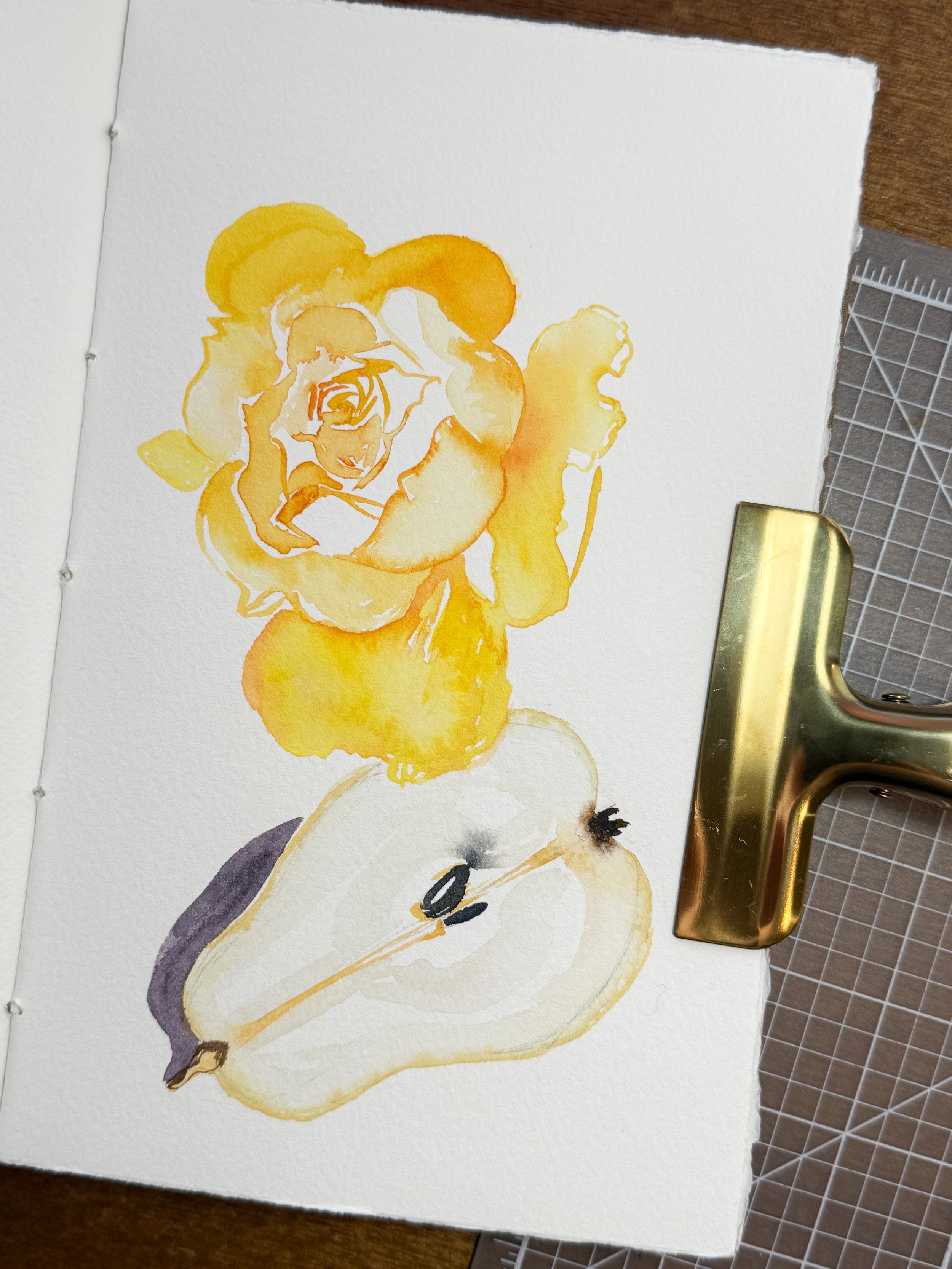 Watercolor painting of a yellow-orange rose flower and a white pear with a leaf, on textured white paper.