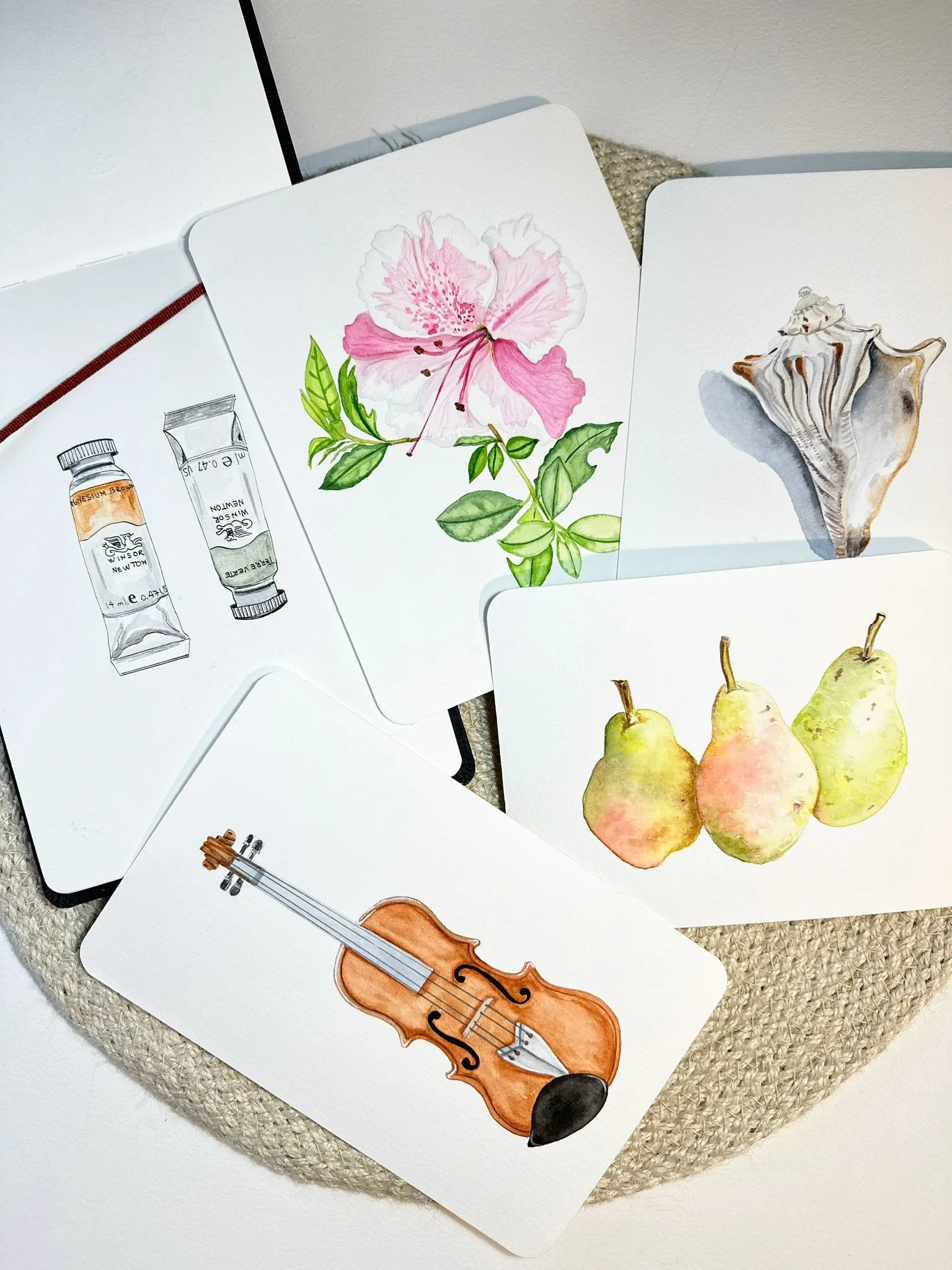A set of illustrated cards featuring a rose flower, a seashell, three pears, a violin, and two paint tubes, arranged on a textured surface.