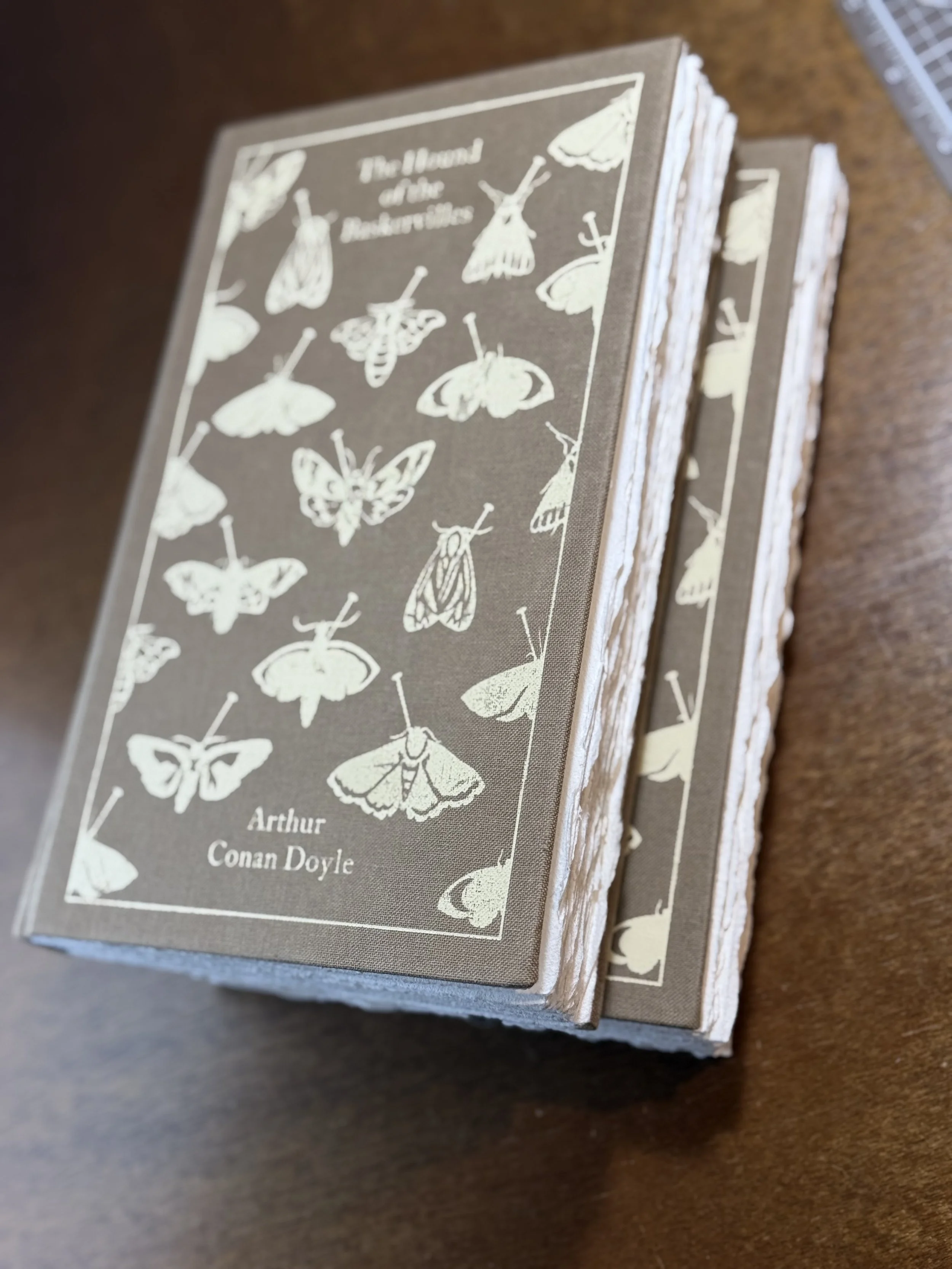 A stack of books with a textured cover featuring illustrations of various moths, titled "The Moth” by Arthur Conan Doyle.